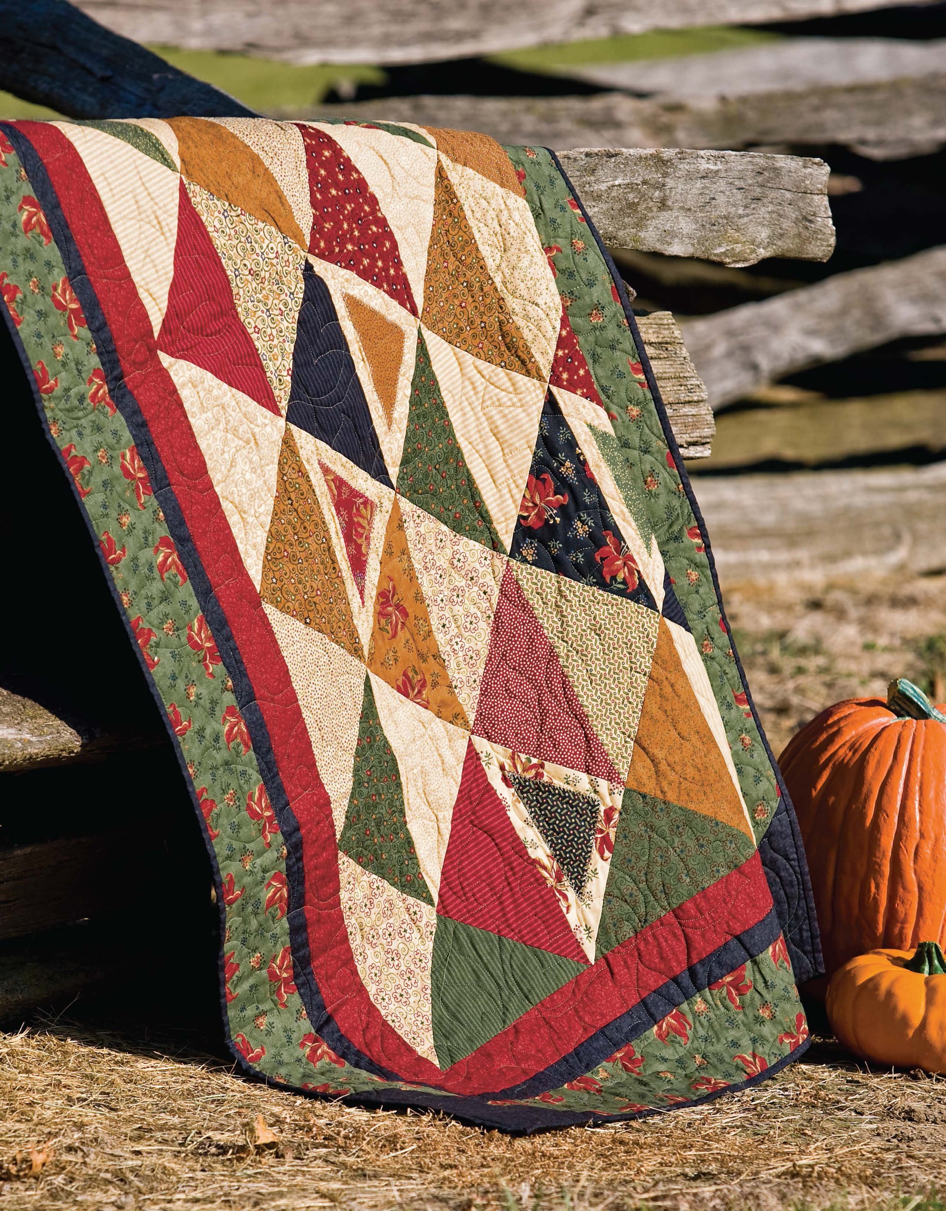 The Lap & Throw Quilts by Leisure Arts features a vibrant triangle patchwork in red, green, gold, and beige draped over a rustic wooden fence with an orange pumpkin nearby—perfect inspiration for beginner quilting projects.