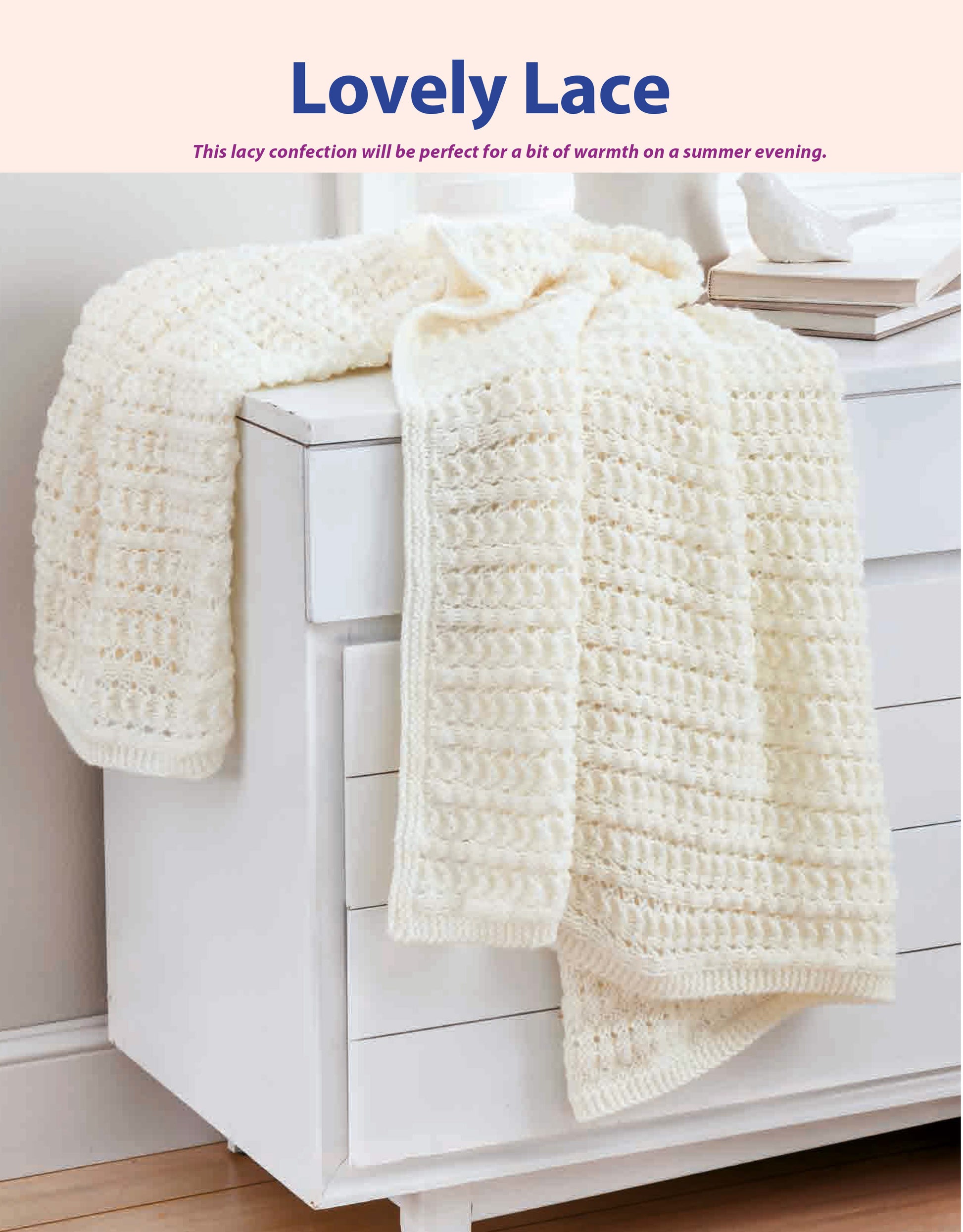 A soft, lacy white knitted blanket made with Beginner-Friendly Knitting by Leisure Arts is draped over a white dresser in a cozy, softly lit room.