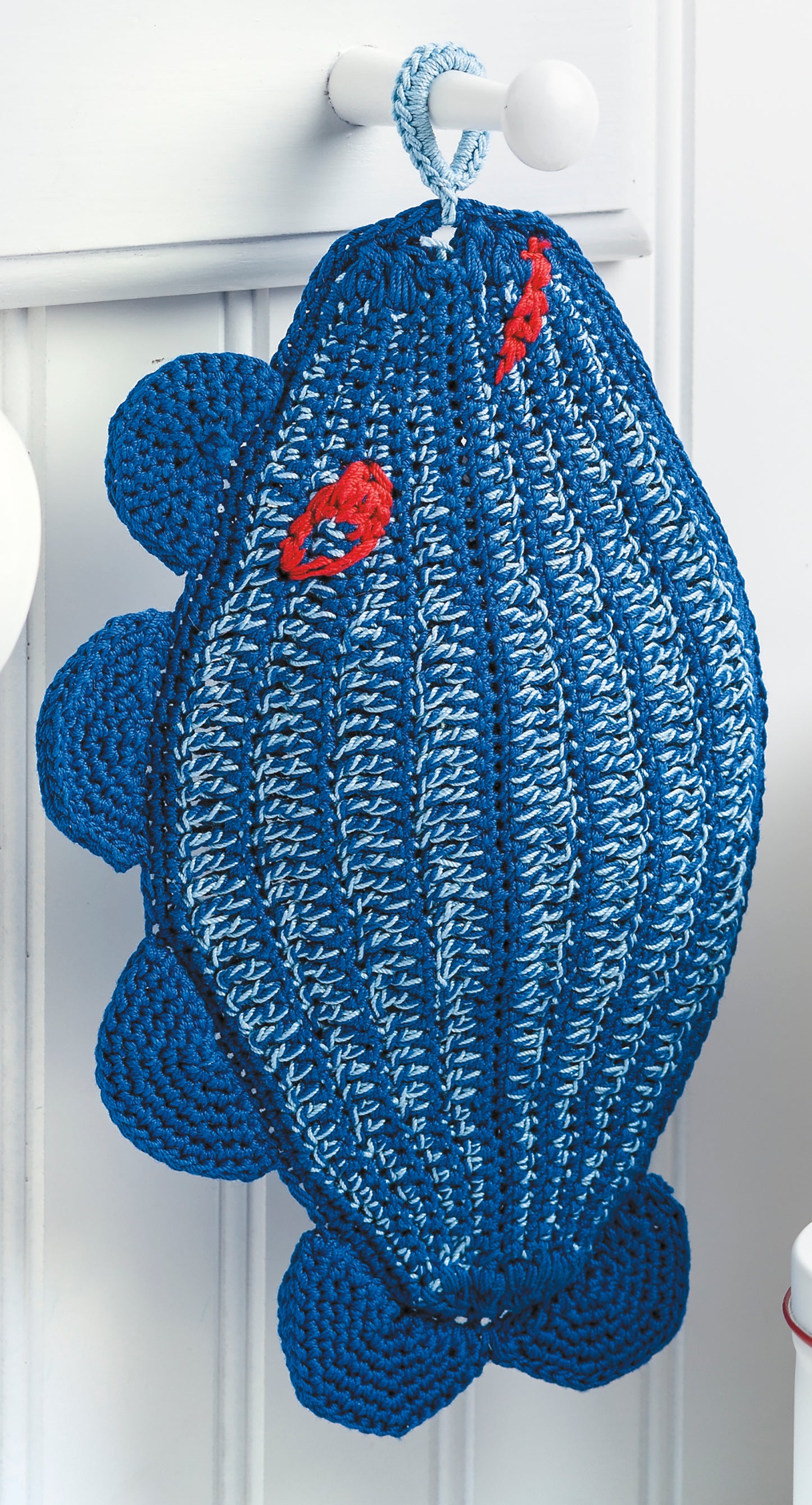 The Leisure Arts Potholders & Dishcloths Digital Download features a blue and light blue fish-shaped crocheted potholder with red embroidered accents, displayed hanging from a white knob on a white background.
