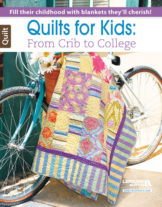 A pastel baby quilt with playful patterns is draped over a white bike and basket of daisies. Text: Quilts for Kids—From Crib to College by Leisure Arts—the ideal beginner quilting book.