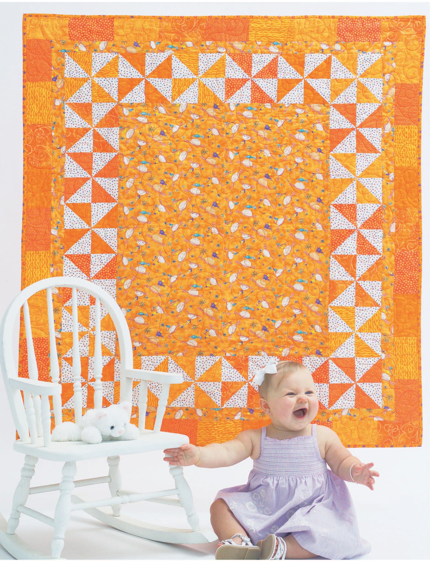 A smiling baby in a lavender dress sits by a white chair with a stuffed animal, in front of an orange and white quilt inspired by beginner patterns from "Quilts for Kids—From Crib to College" by Leisure Arts.