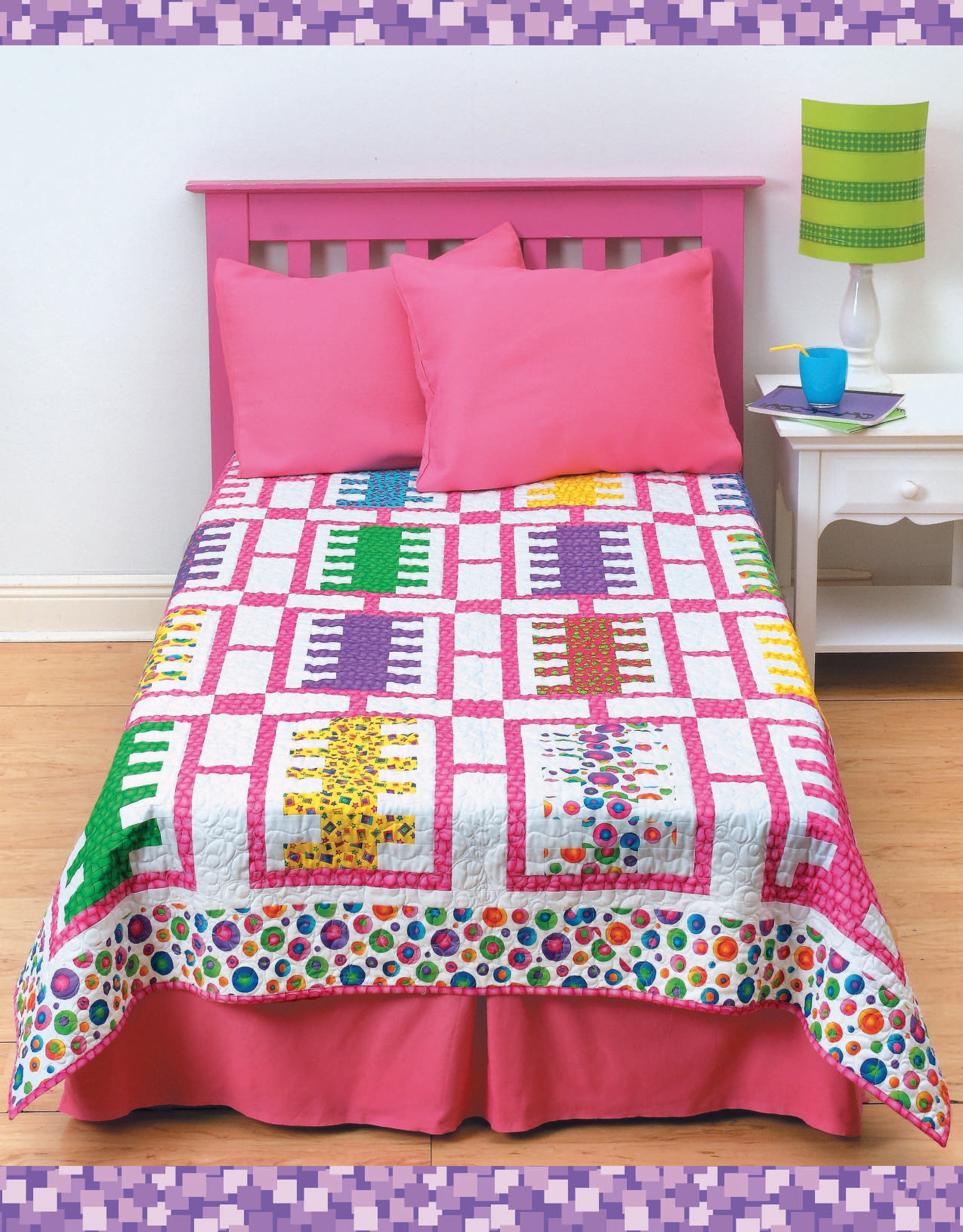 A bed features a pink headboard, two pink pillows, and bedding with the Leisure Arts "Fun Colorful Quilts Digital Download." Beside it is a white nightstand holding a green-striped lamp, a book, and a blue cup.