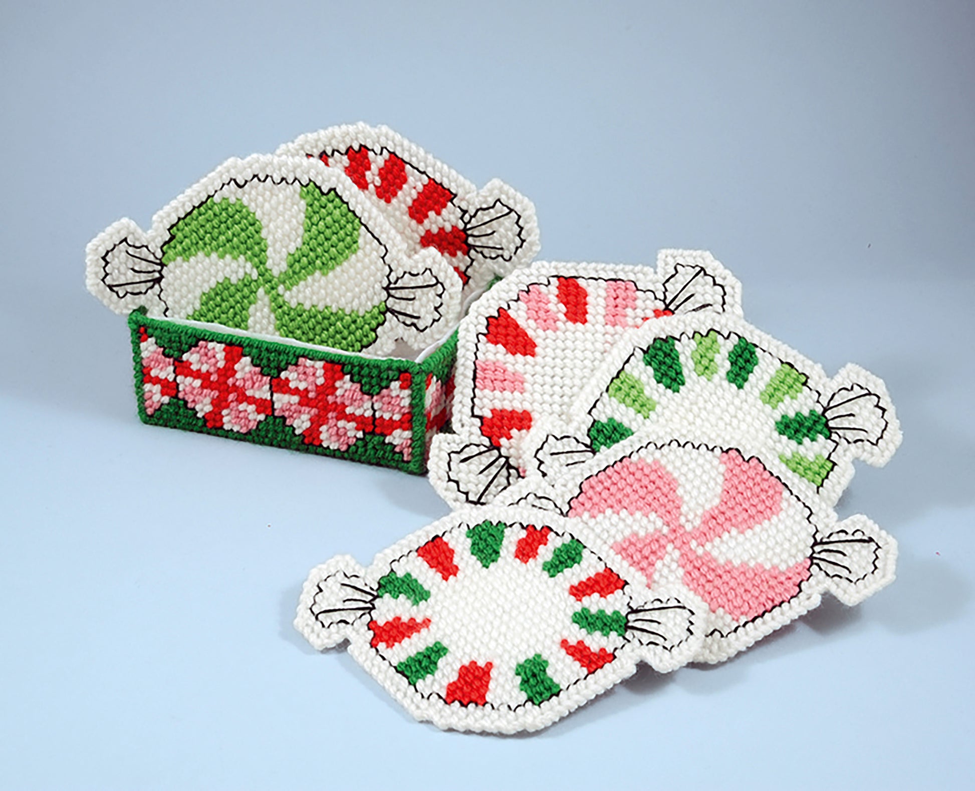 Leisure Arts Coasters and Lollipop Covers feature red, green, and pink peppermint-inspired designs with holiday motifs and a floral holder. Crafted from plastic canvas and yarn for a handmade look, they're ideal festive gift accents.