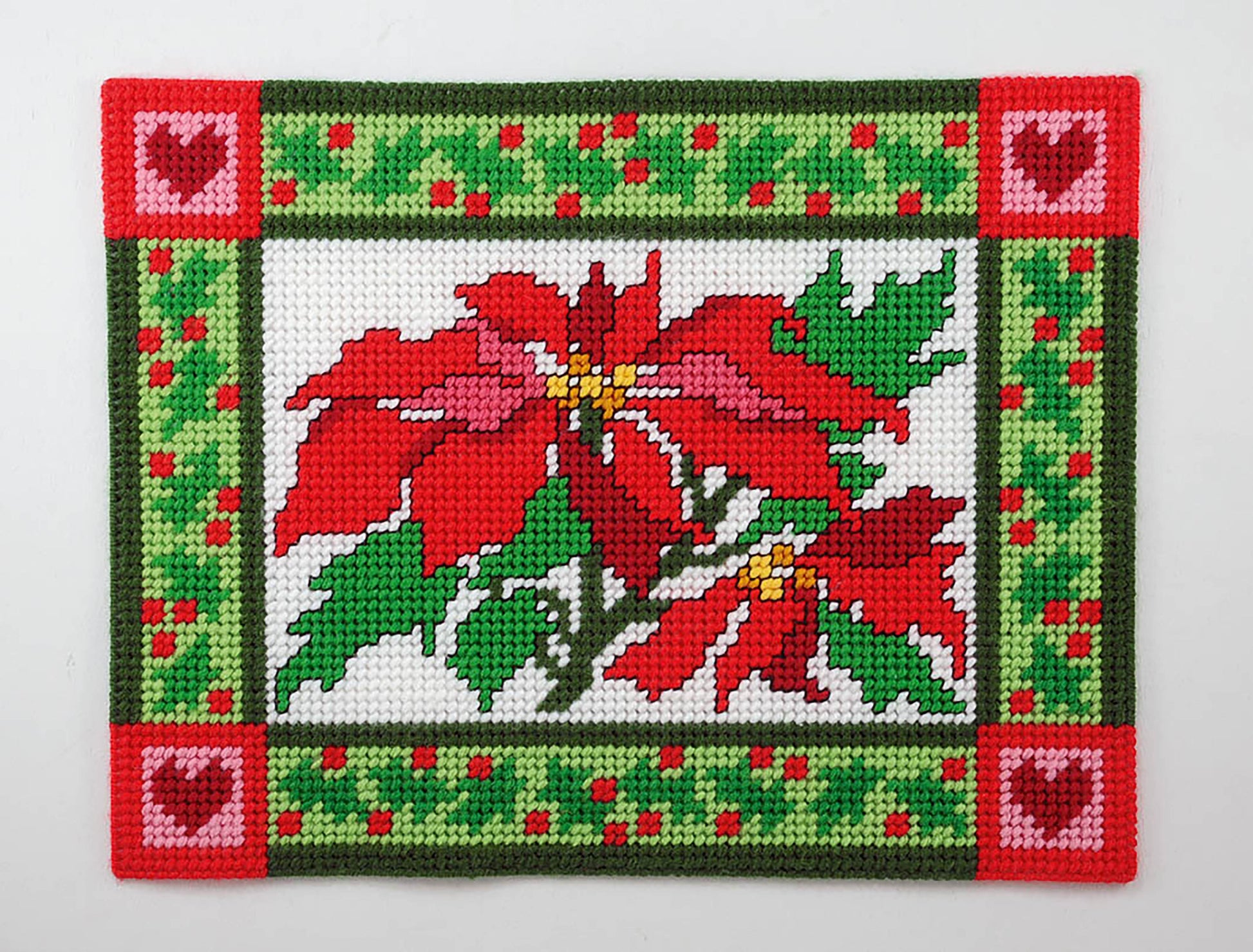 The Leisure Arts Party Place Mats are rectangular holiday needlepoint mats featuring red poinsettias, festive borders, heart corners, and berry accents—perfect as plastic canvas place mats for holiday celebrations.