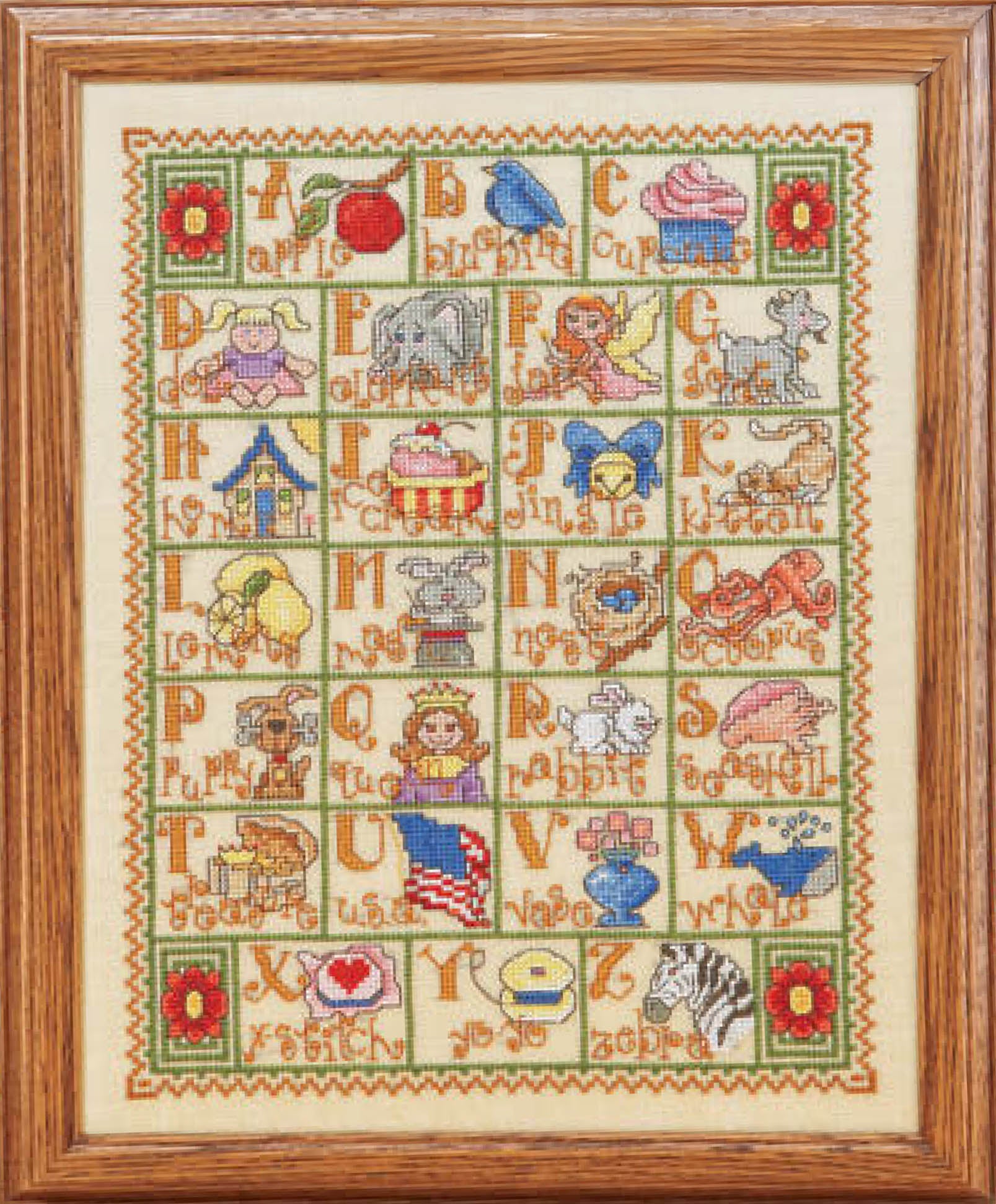 The Leisure Arts A to Z Alphabets Cross Stitch features framed alphabet lettering, each letter with a vibrant object or animal, and is finished with a green and red floral border.
