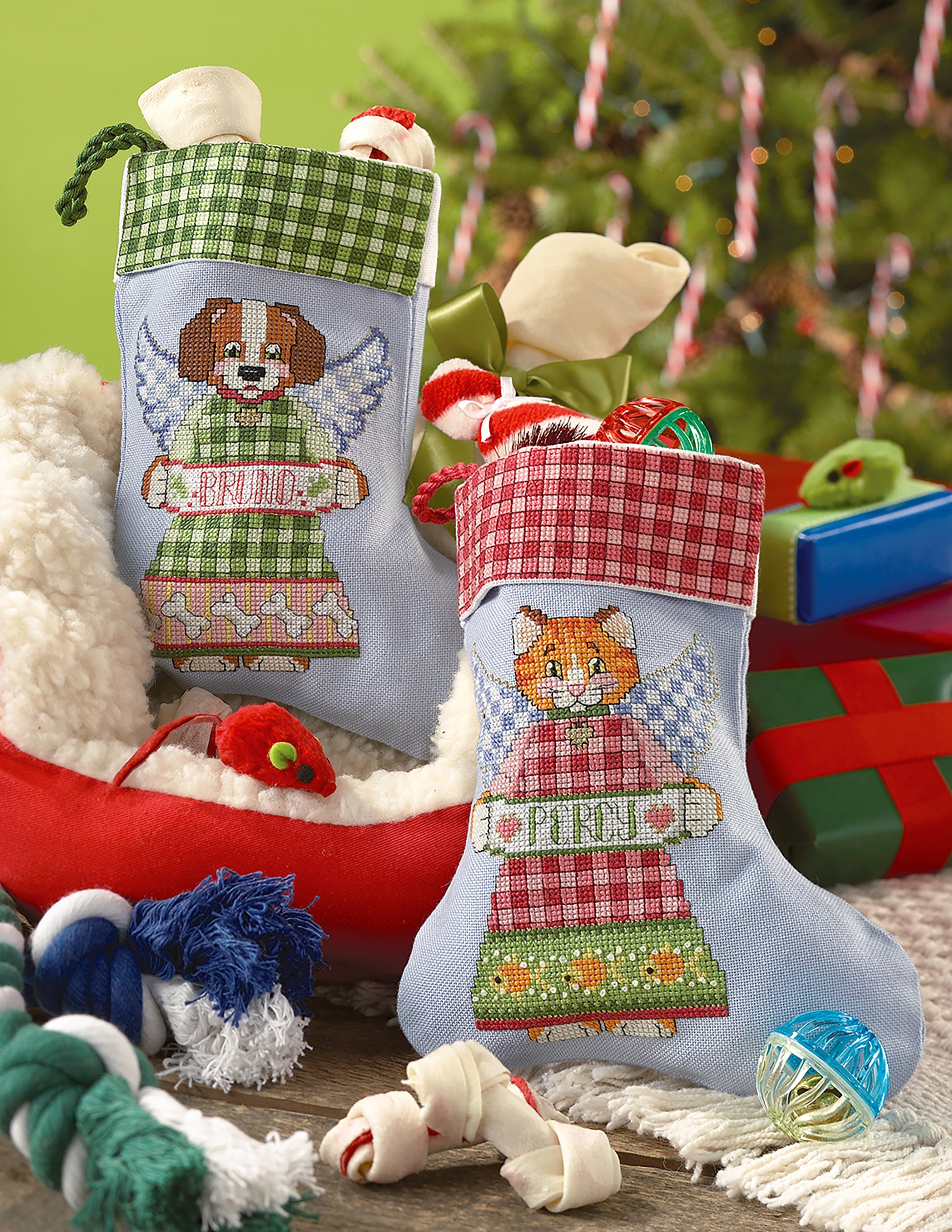 Leisure Arts Christmas Stockings for beginners, personalized for BRUNO and PURDY, showcase cute dog and cat angels. Filled with toys and treats, they sit in front of a decorated Christmas tree.
