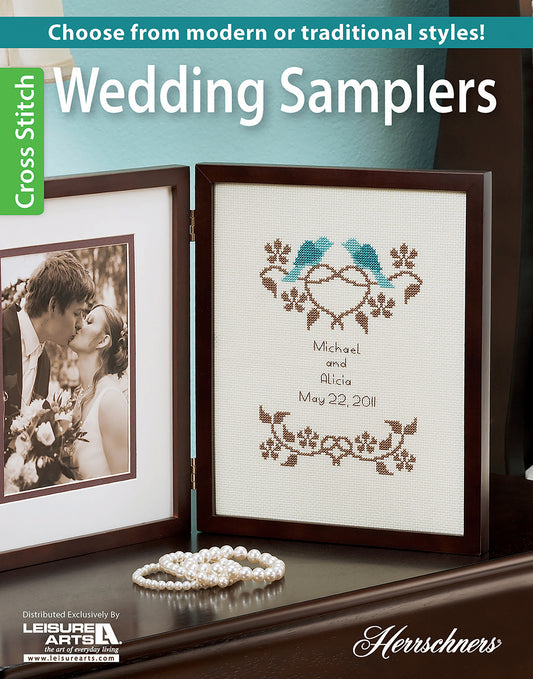 A framed “Wedding Samplers—Choose From Modern or Traditional Style!” by Leisure Arts with birds and floral designs sits beside a couple’s photo, a pearl necklace, and a turquoise wall—an ideal handmade wedding keepsake.
