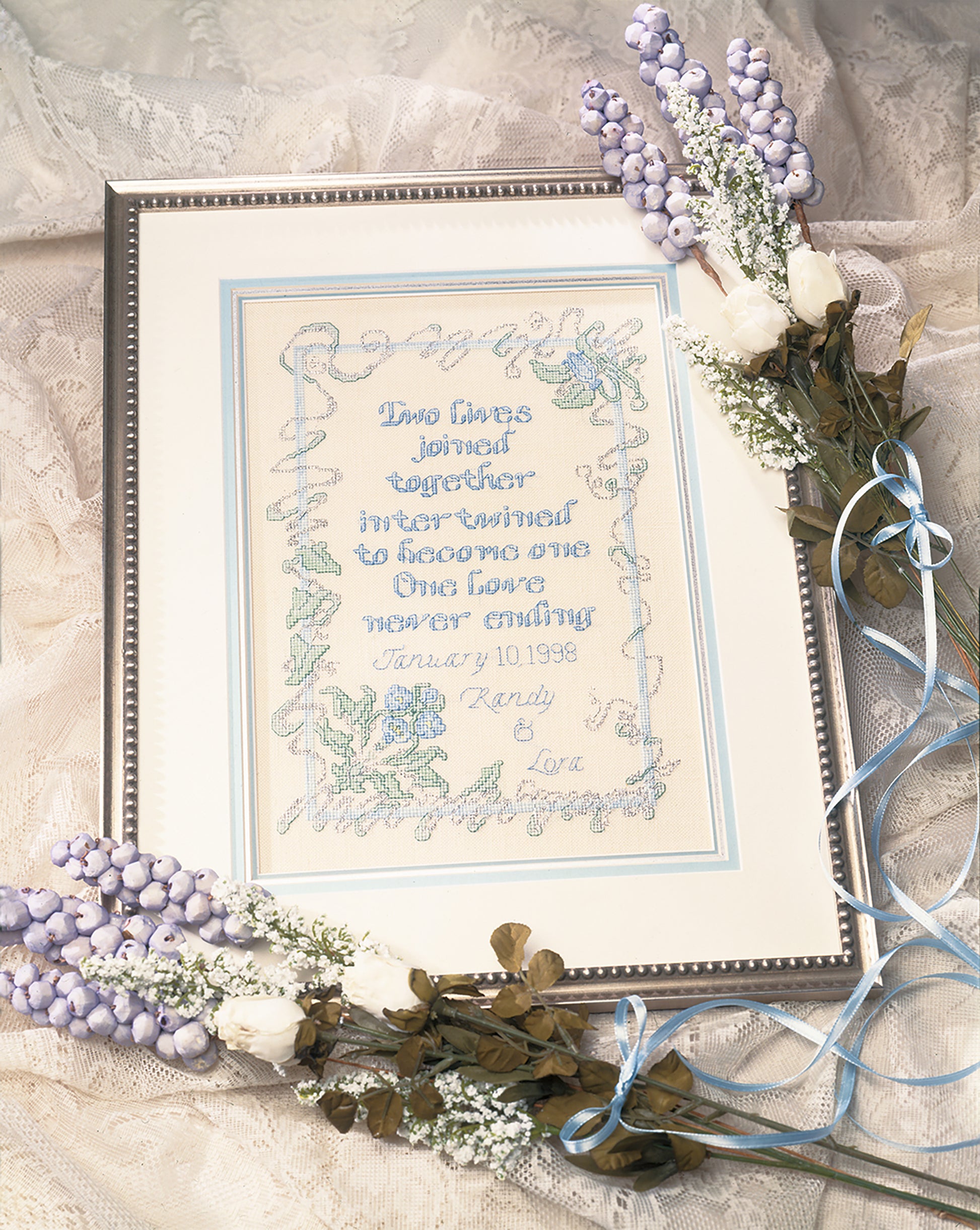 The Leisure Arts Wedding Samplers—Choose From Modern or Traditional Style! feature romantic poems and wedding dates, accented with blue and white faux flowers and ribbons for a charming handmade keepsake on lace.