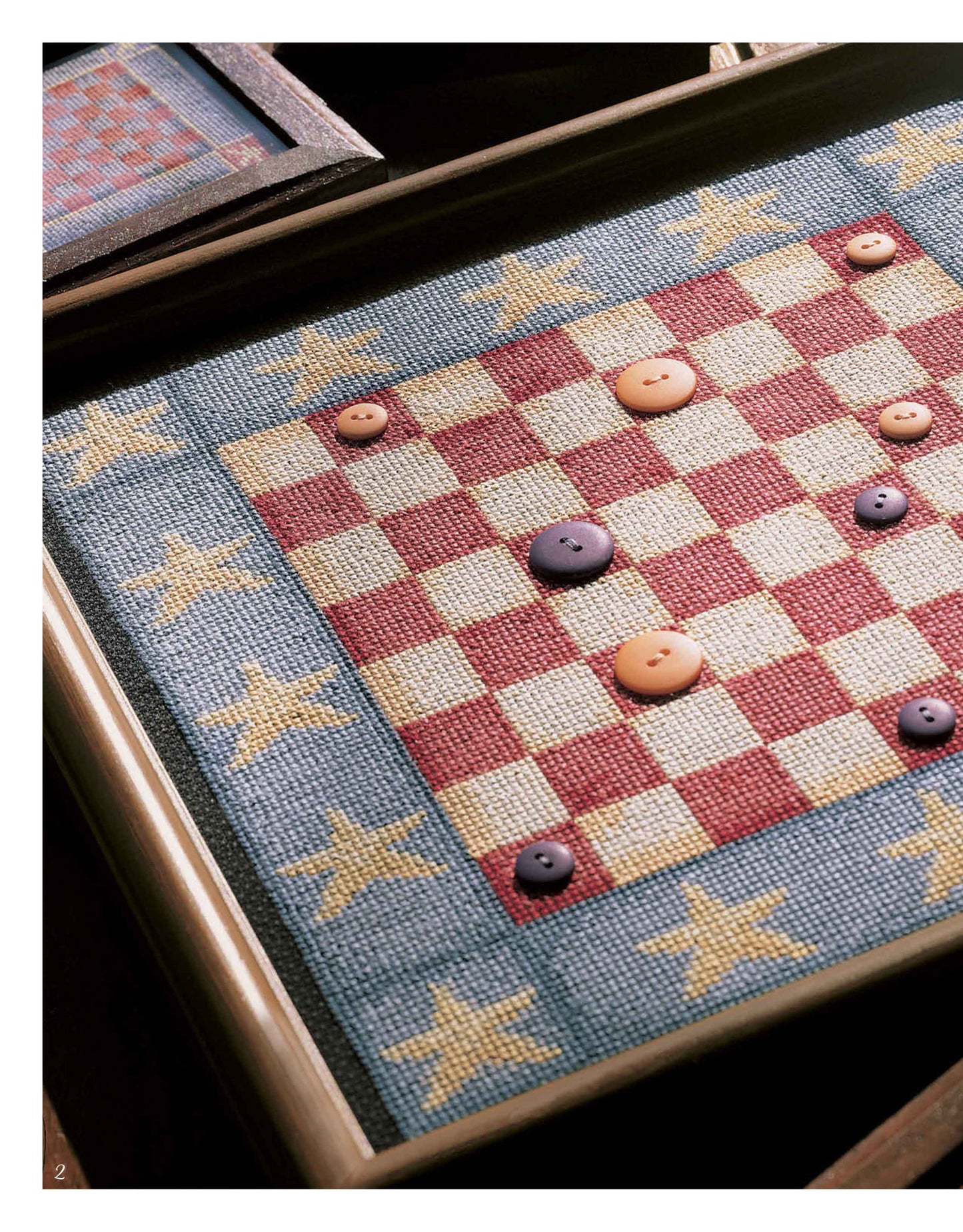 The Leisure Arts Antique Game Board Set features a framed red and white checkerboard with a blue border and yellow stars, plus button playing pieces, all in a patriotic, folk-art style inspired by vintage designs.