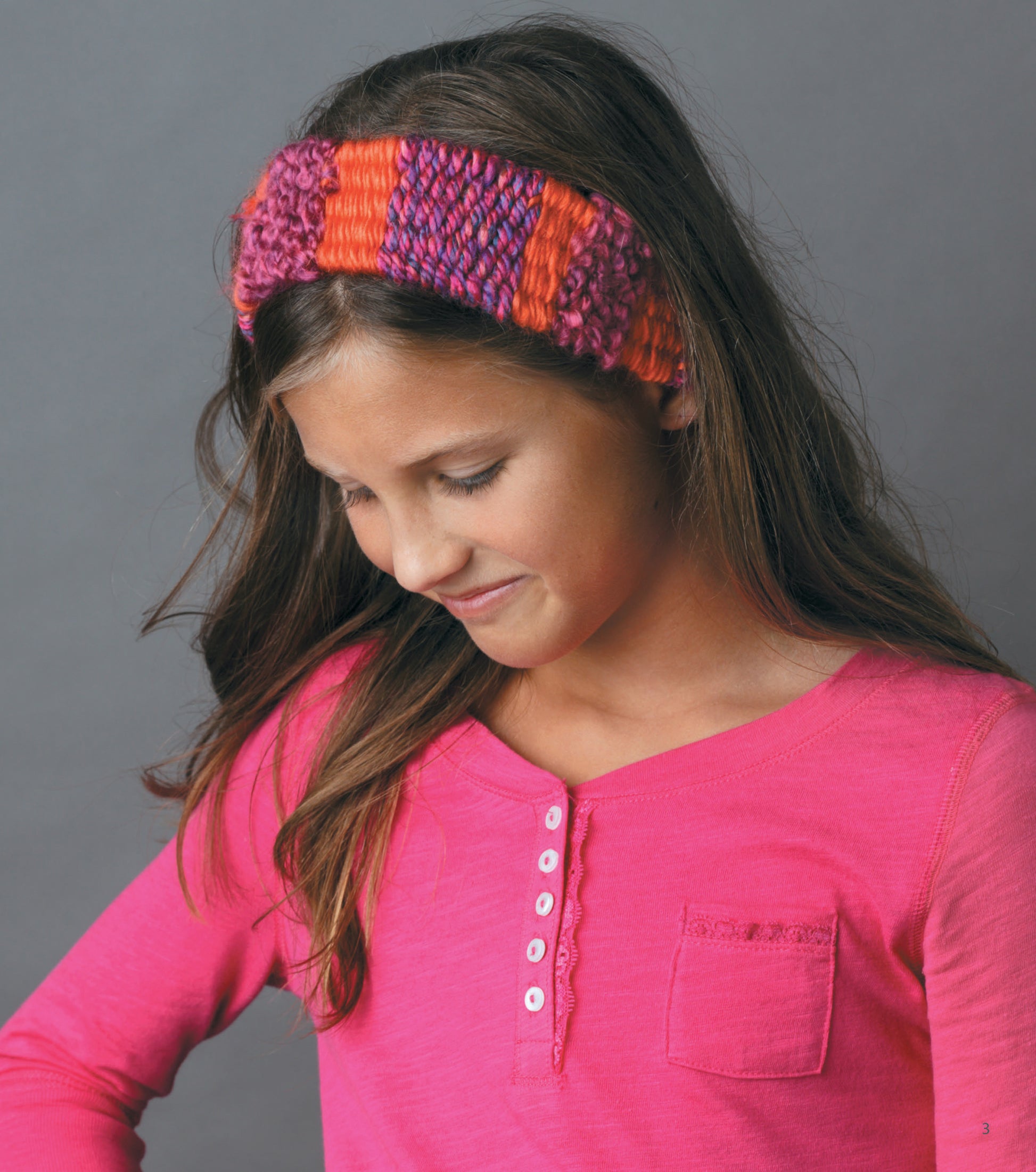 A young girl in a pink long-sleeve henley smiles softly, wearing a striped beginner headband she made with Leisure Arts’ The Dream Weaver—A Simple Way to Weave Anything You Can Imagine.