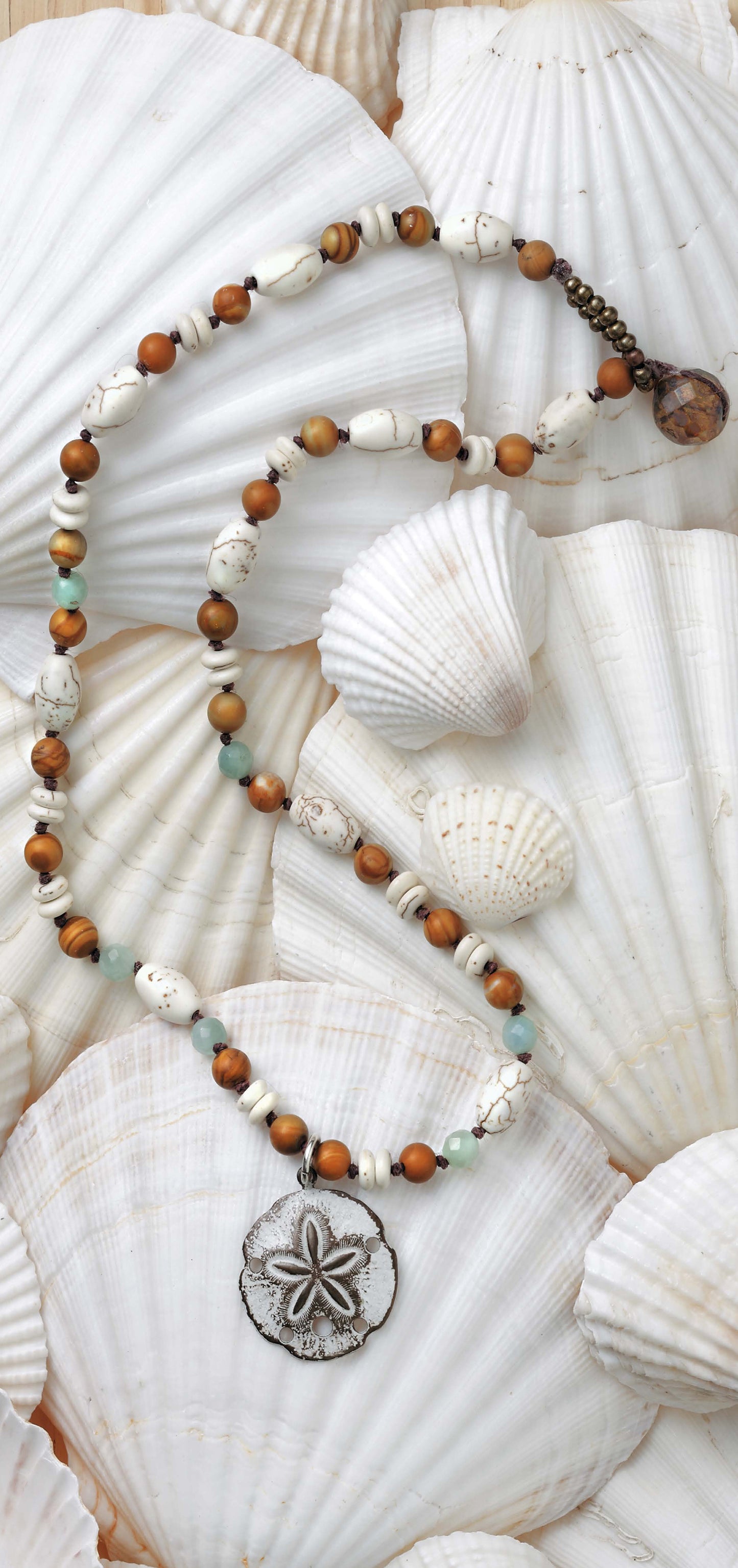 Leisure Arts' Beach Chic Jewelry features a coastal necklace with white, brown, and turquoise beads plus a silver sand dollar pendant, displayed on overlapping white seashells—ideal for ocean-inspired accessory lovers.