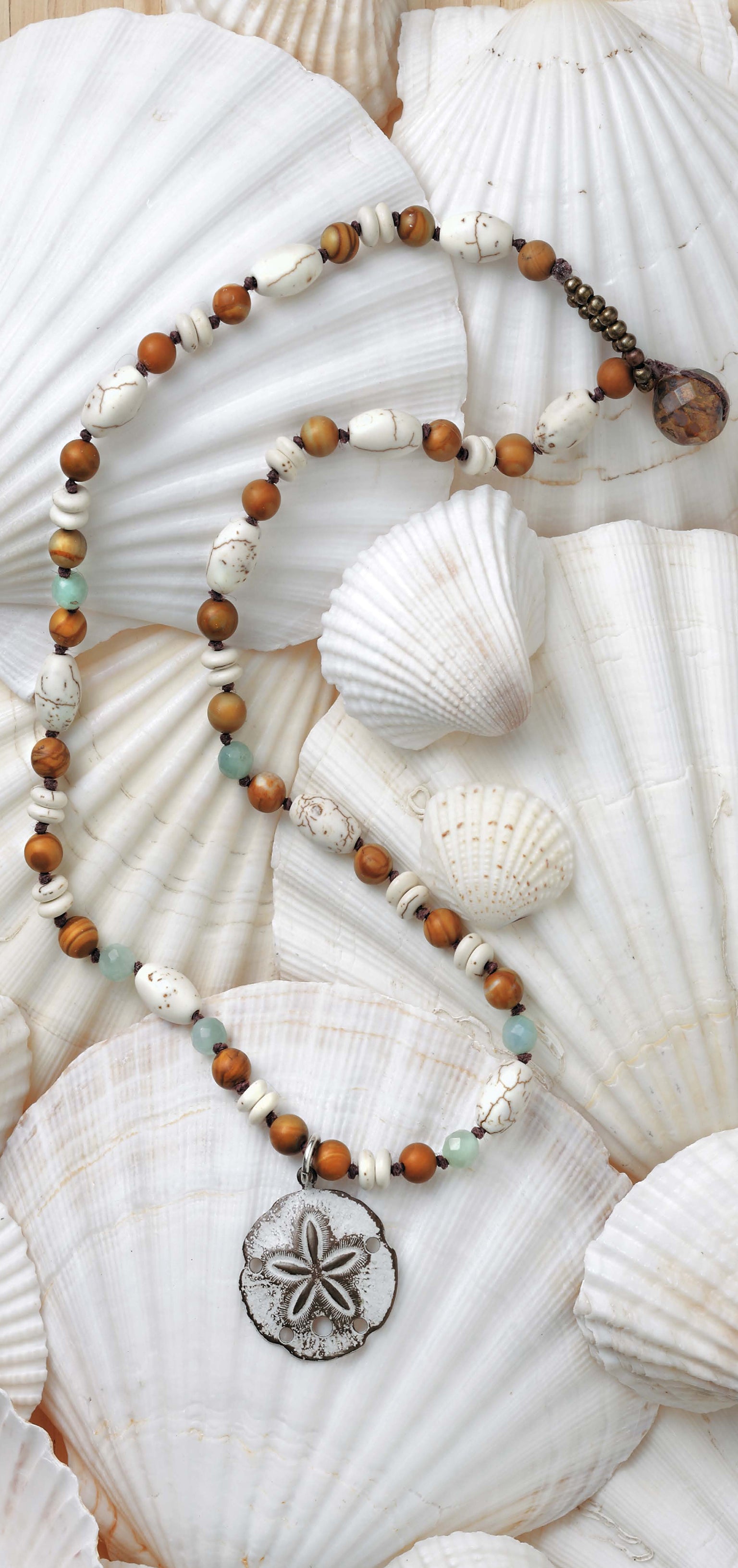 Leisure Arts' Beach Chic Jewelry features a coastal necklace with white, brown, and turquoise beads plus a silver sand dollar pendant, displayed on overlapping white seashells—ideal for ocean-inspired accessory lovers.
