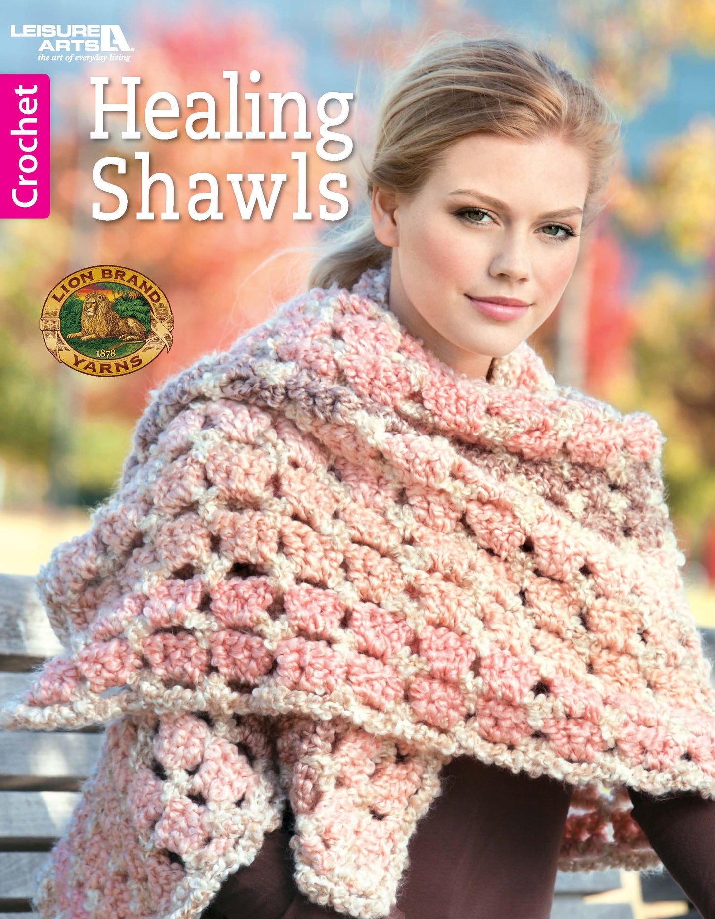 A woman sits outdoors in a chunky pink and cream crochet shawl. The cover reads "Healing Shawls" from Leisure Arts, with autumn leaves in the background—perfect inspiration for cozy crochet gifts or new shawl patterns.