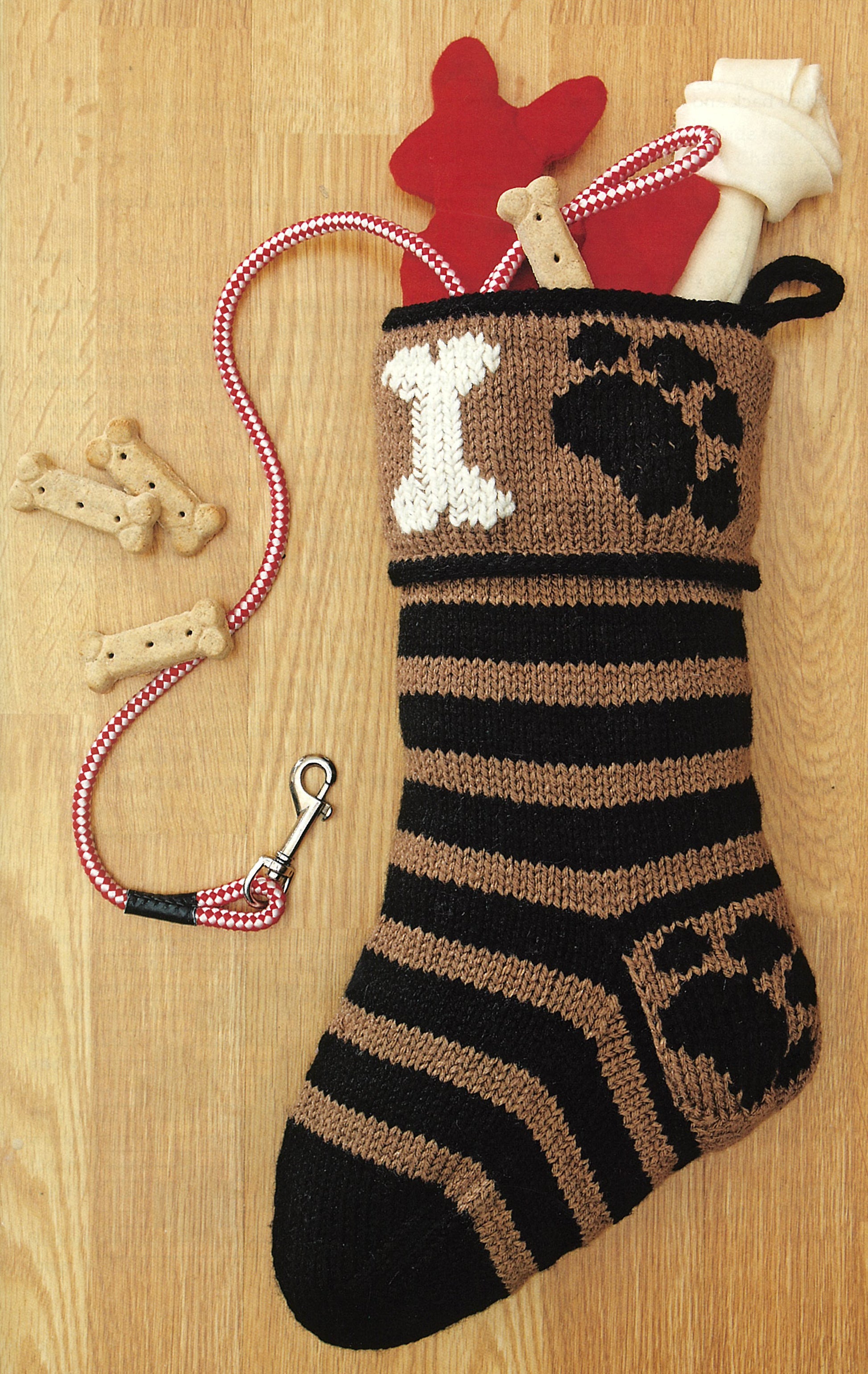 The Stockings Were Knit by Leisure Arts is an intermediate brown and black striped Christmas stocking with a bone and paw print design, perfect for filling with dog treats, toys, or a leash—a festive keepsake for your furry friend.