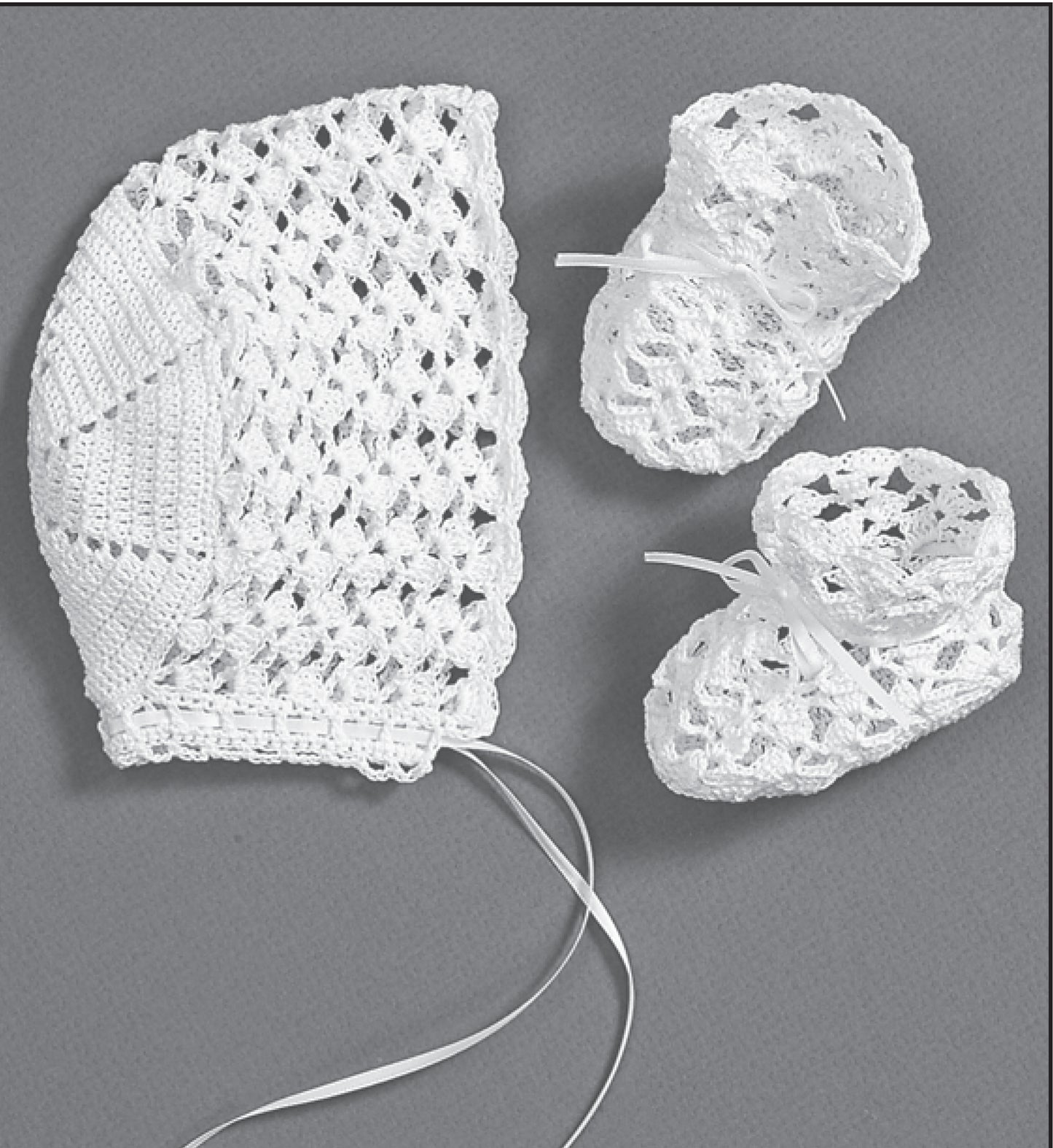 Christening Sets—Celebrate Your Newborn With an Heirloom Outfit! by Leisure Arts: White crocheted baby bonnet and booties with lacy patterns and ribbon ties, ideal for a special christening or as a cherished baby keepsake.