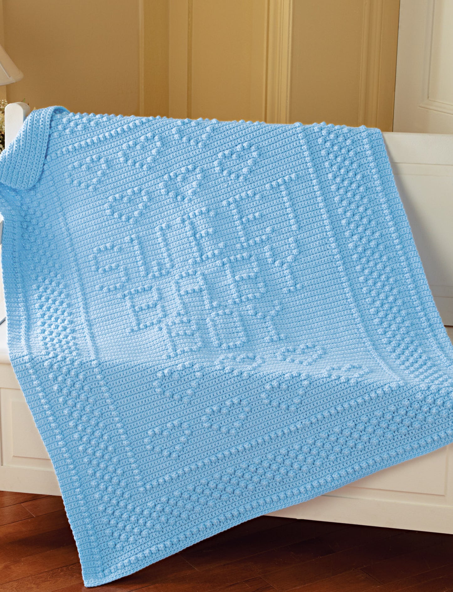 A light blue knitted baby blanket from Terrific-to-Touch Baby Afghans—The Best of Mary Maxim by Leisure Arts, draped over a white crib with raised "SWEET BABY BOY" text, bordered hearts, and perfect for adding charm to any nursery.