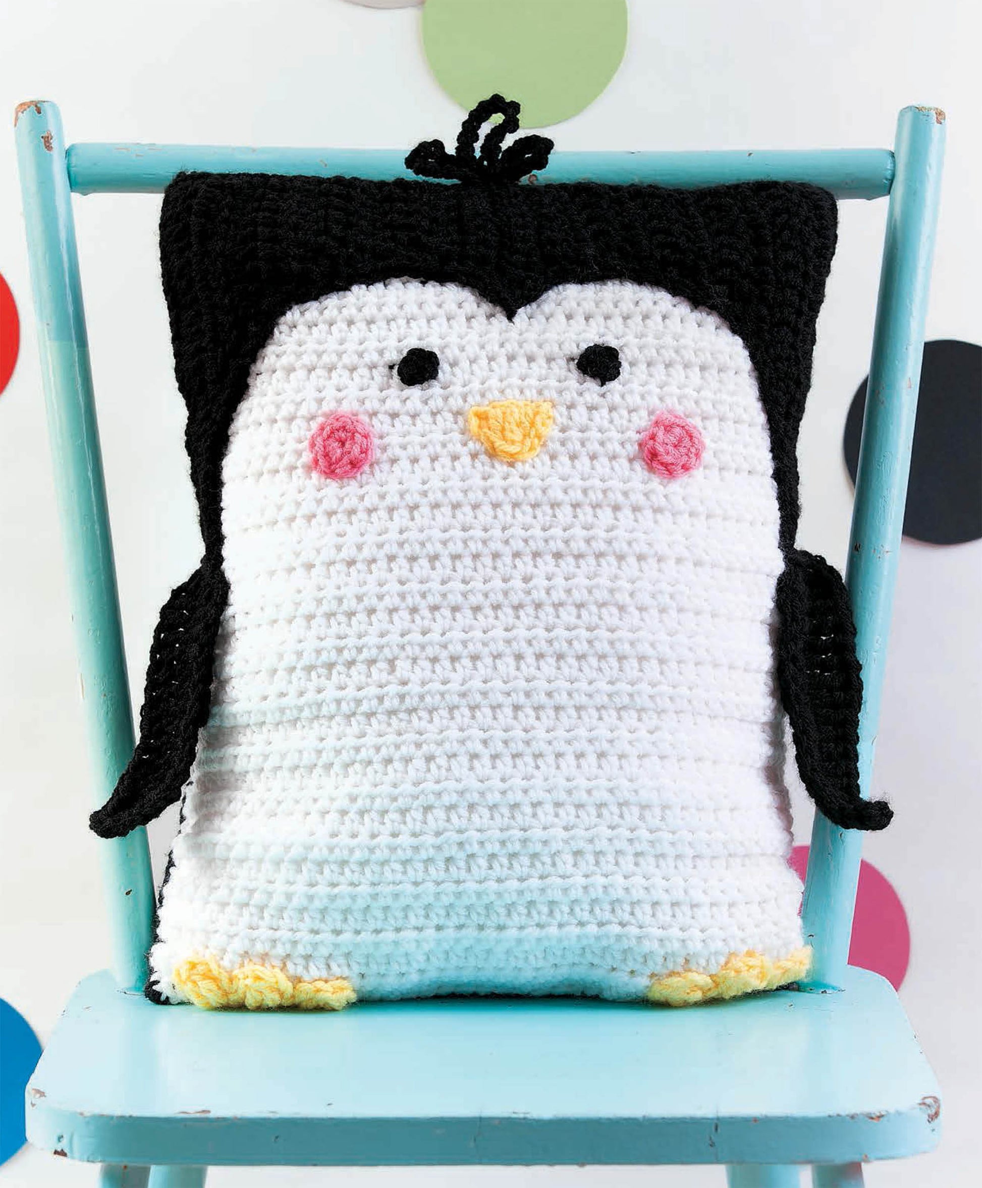 The Leisure Arts Kids Animal Pillows, including an adorable crocheted penguin, add a playful touch to any space—perfectly displayed on a light blue chair against a white backdrop with colorful polka dots.