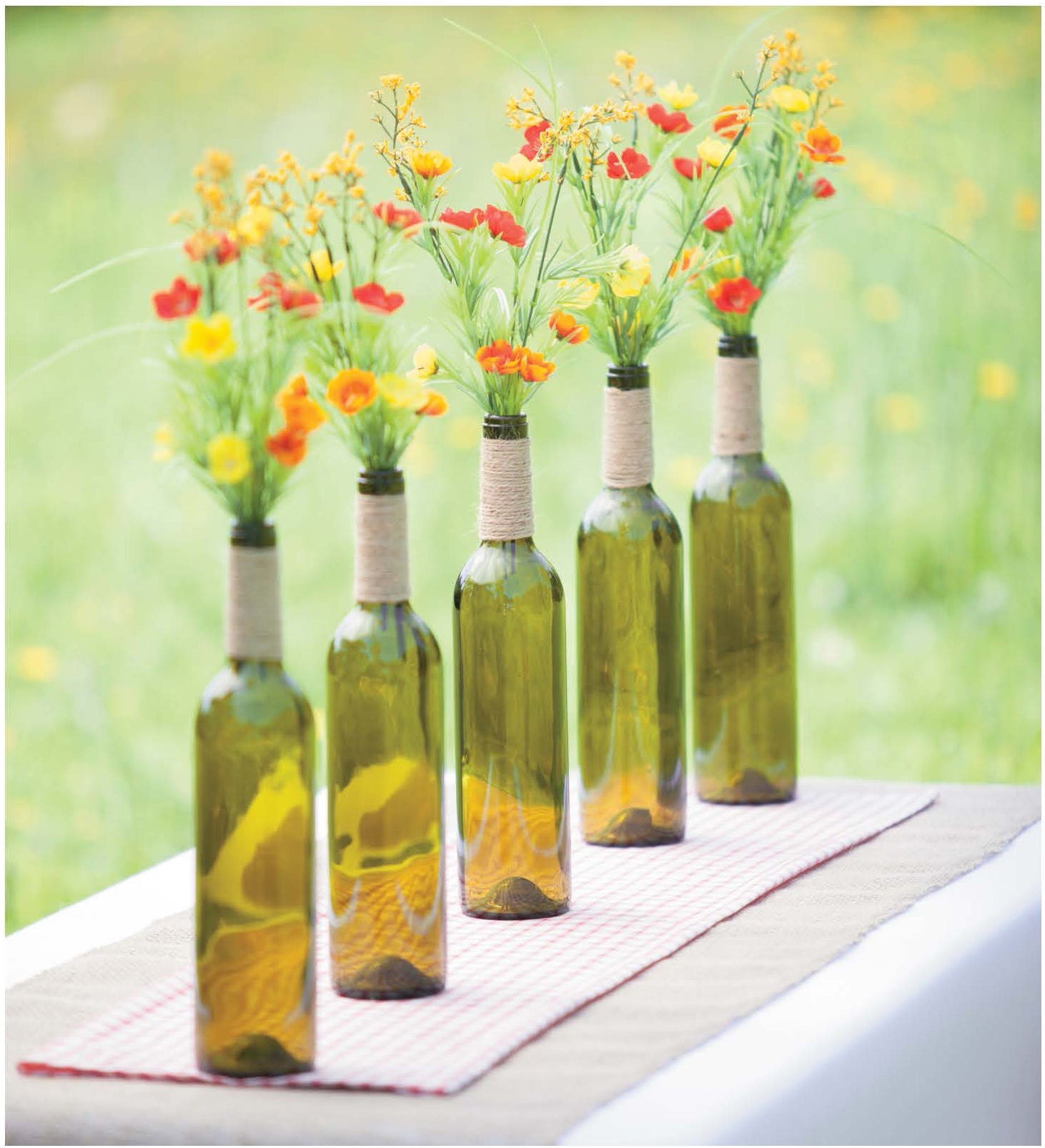 Rustic Wedding Florals by Leisure Arts features five green glass bottles with twine-wrapped necks and bright artificial flowers—ideal for rustic wedding ideas or charming country wedding decorations outdoors.