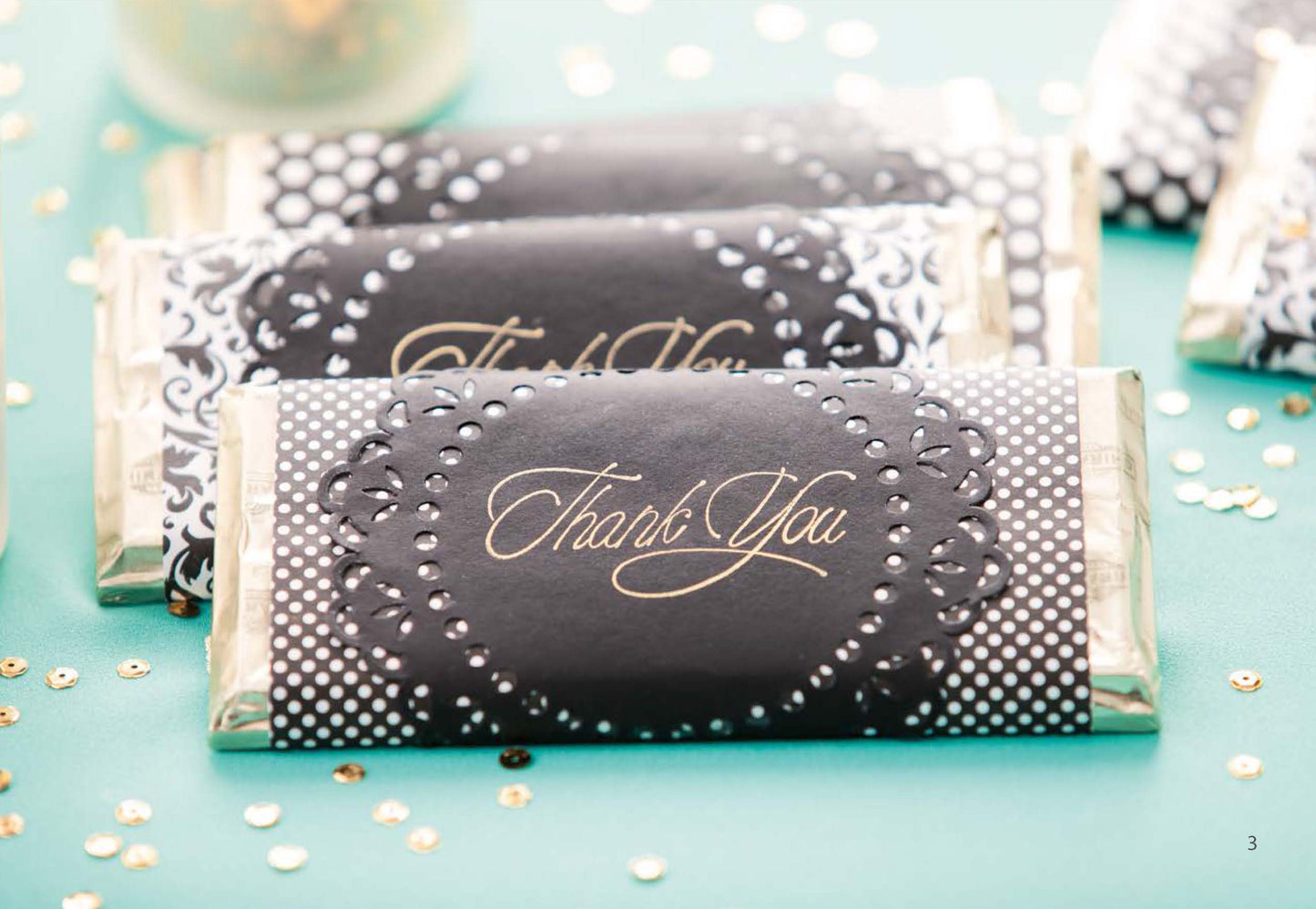 The Glam Wedding Favors Digital Download by Leisure Arts features chocolate bar wrappers in elegant black and white with gold “Thank You” text, ideal for wedding favors and display among gold and white confetti.
