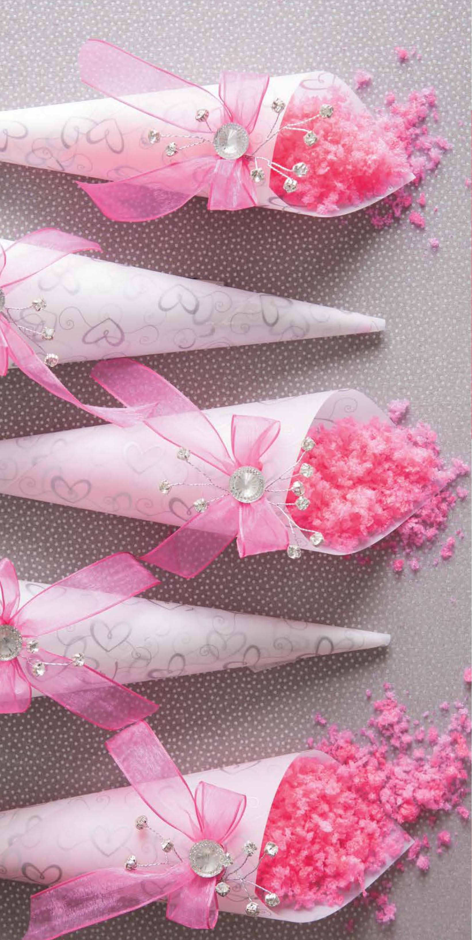 The Glam Wedding Favors Digital Download by Leisure Arts features five paper cones with pink ribbons, silver gems, and heart patterns, filled with pink confetti—perfect for charming DIY gifts or favors, beautifully arranged with some confetti spilling out.
