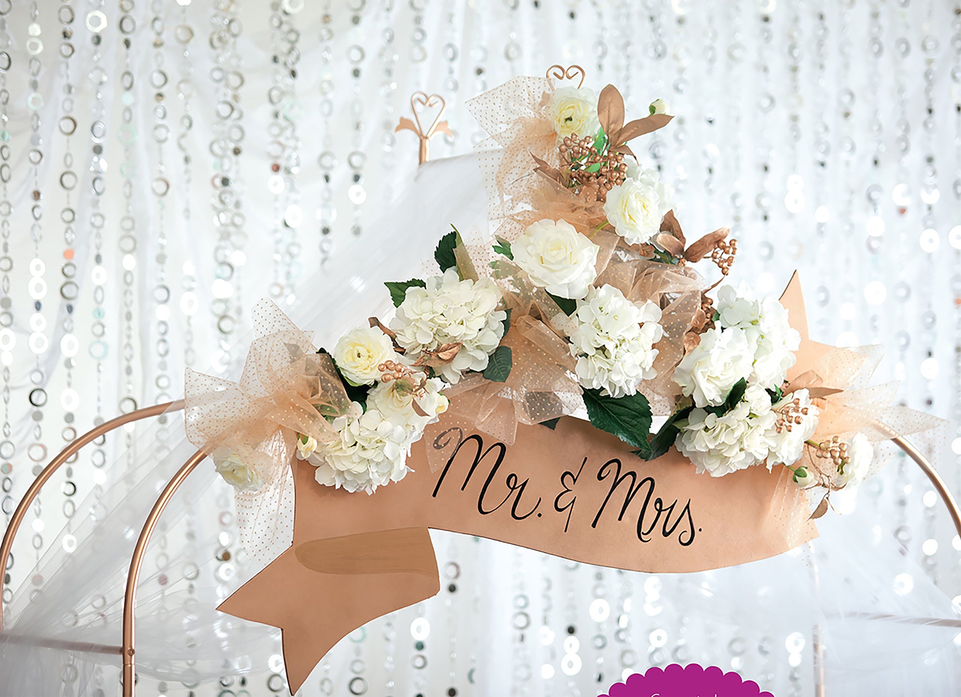 Glam Wedding Florals by Leisure Arts features white roses, hydrangeas, gold mesh ribbons, and a "Mr. & Mrs." banner on a sequin backdrop—ideal for DIY wedding decor or beginners learning floral arrangement basics.
