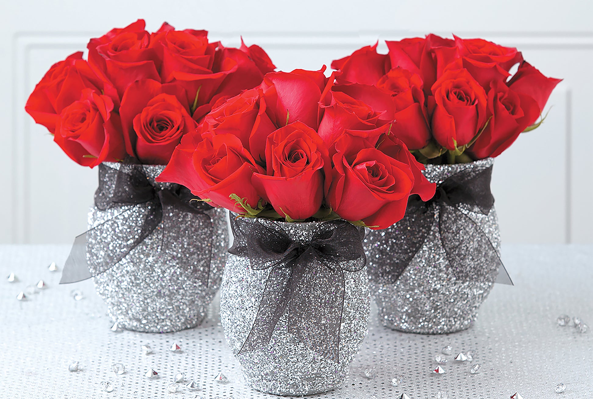 Glam Wedding Florals by Leisure Arts features glittery silver vases filled with red roses and black ribbon, perfect for chic DIY wedding decor on a white surface with decorative gems.