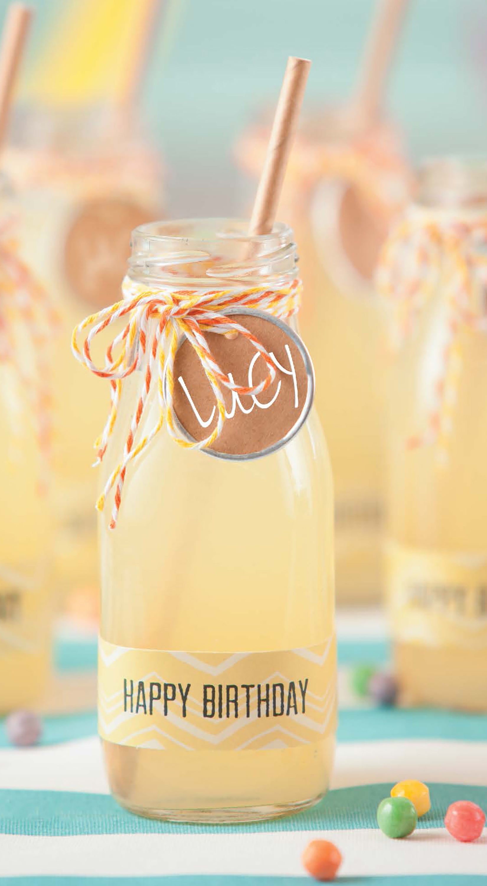 Celebrate birthdays with Leisure Arts’ "Celebrate Birthdays—Create Fun for Kids or Adults with Unique DIY Party Crafts!" Featuring a glass bottle of yellow lemonade, striped straw, Lucy tag, Happy Birthday label, plus candies and playful party decor.