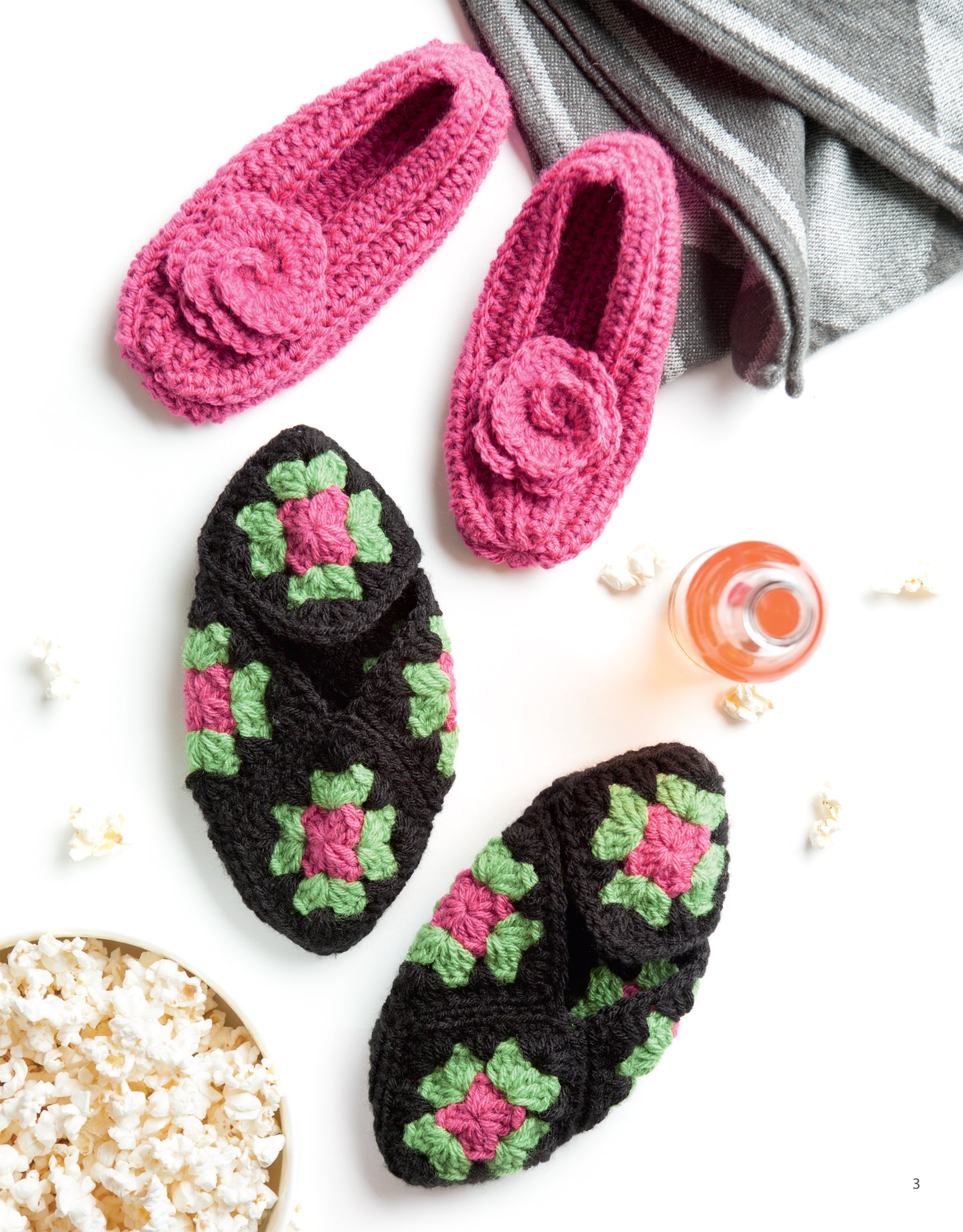 Leisure Arts’ “Slipper for the Family Digital Download” features two pairs of crocheted house slippers—one pink with a flower and one black with green and pink squares—shown beside cozy accents on a white background.