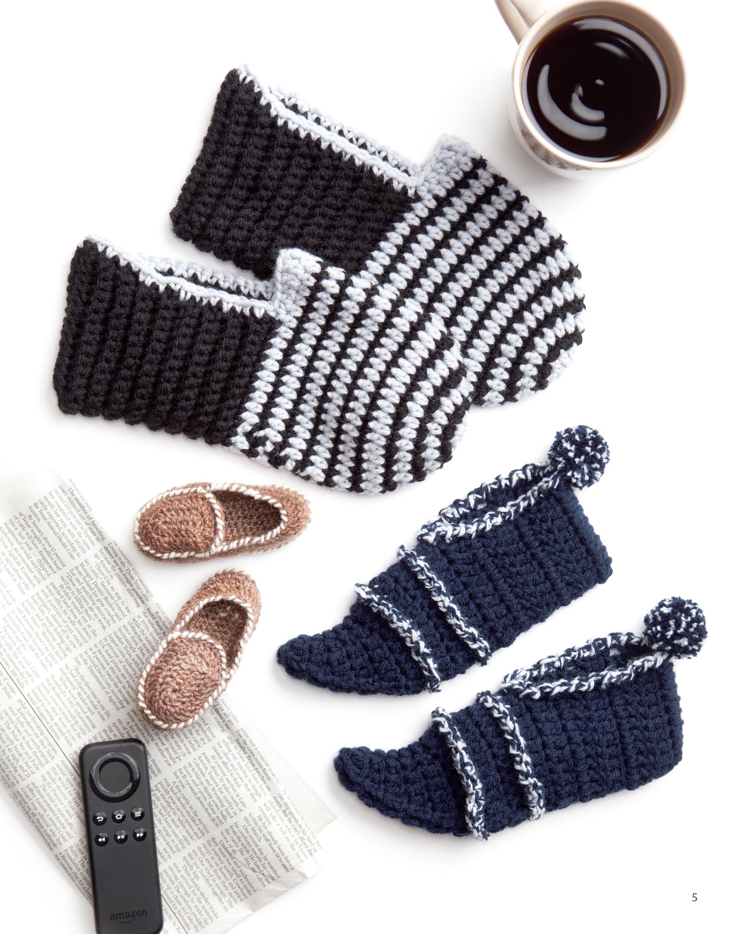 Leisure Arts' Slipper for the Family Digital Download features cozy knitted house shoes in black, white, navy with pom-poms, and tiny brown crocheted slippers—perfect beginner crochet projects displayed beside coffee, a remote, and a newspaper.