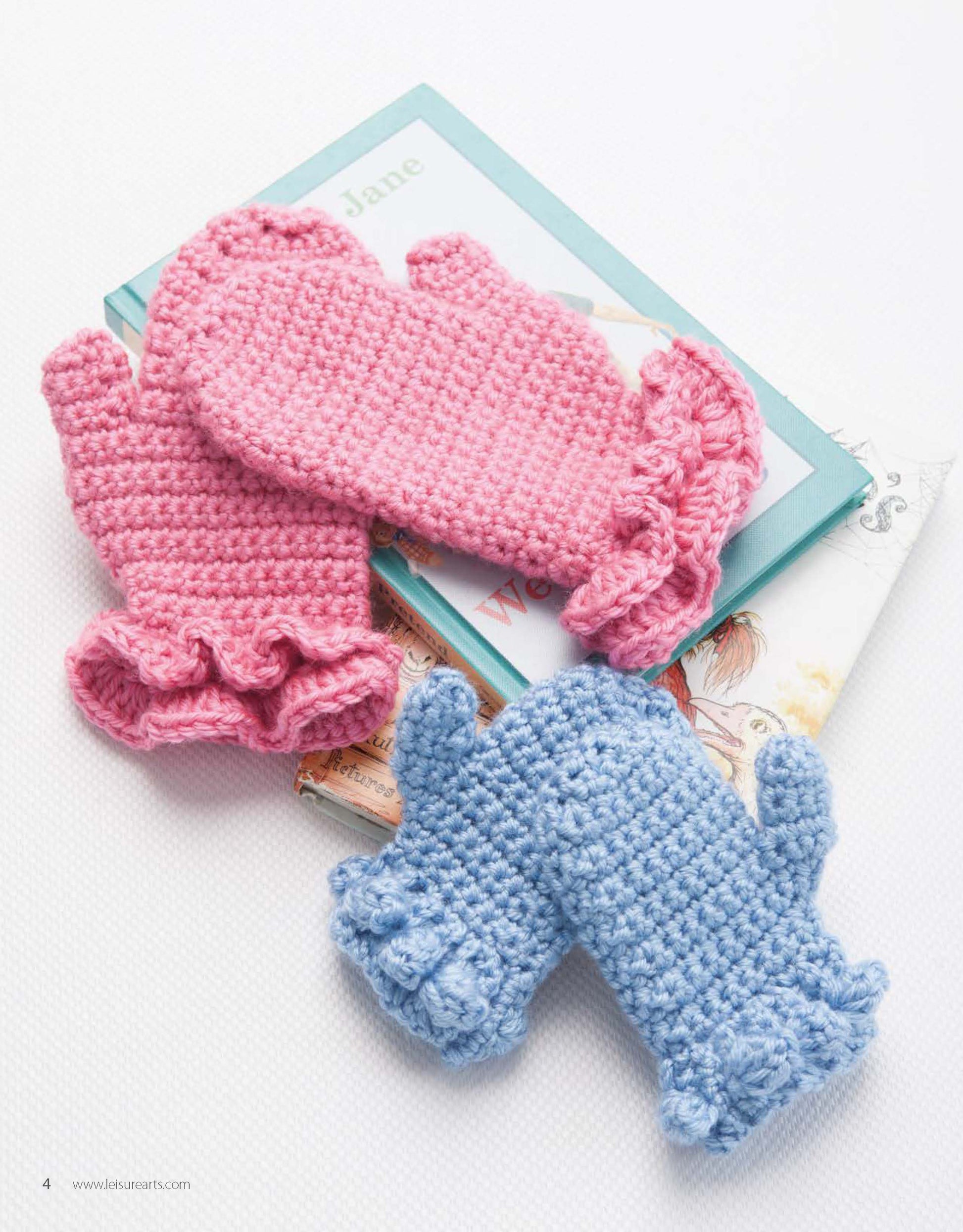 Two pairs from Leisure Arts’ Hand-Picked Gloves & Mitts—one pink with ruffled cuffs and one blue with small bows—are displayed atop a stack of illustrated books.