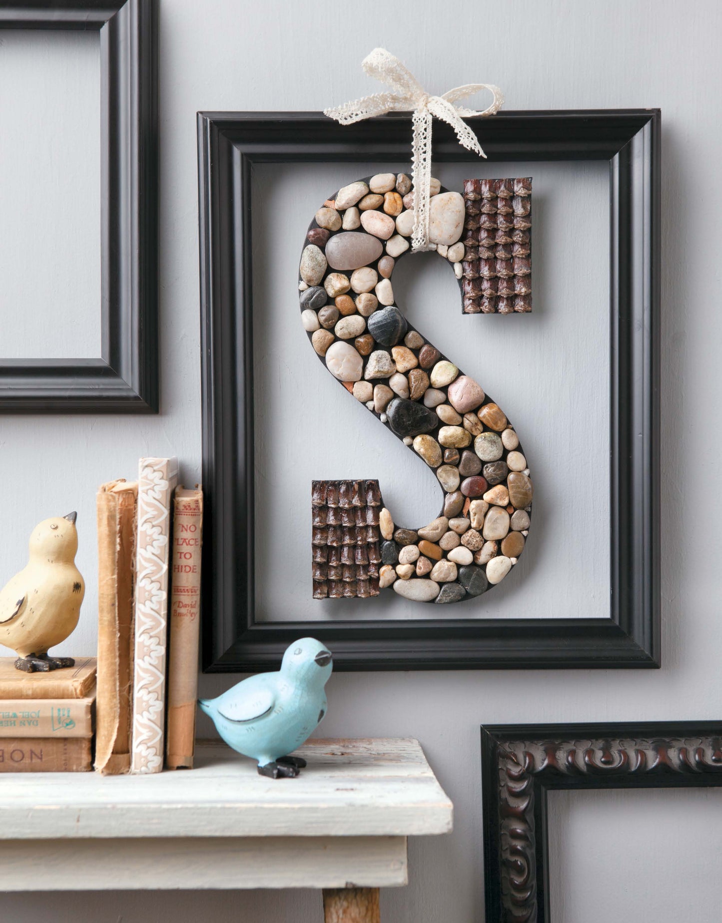 The Decorating Letters Digital Download by Leisure Arts features a framed letter S design with small stones and textured brown squares, perfect for unique home decor paired with birds, vintage books, shelves, and empty frames for a cozy vibe.