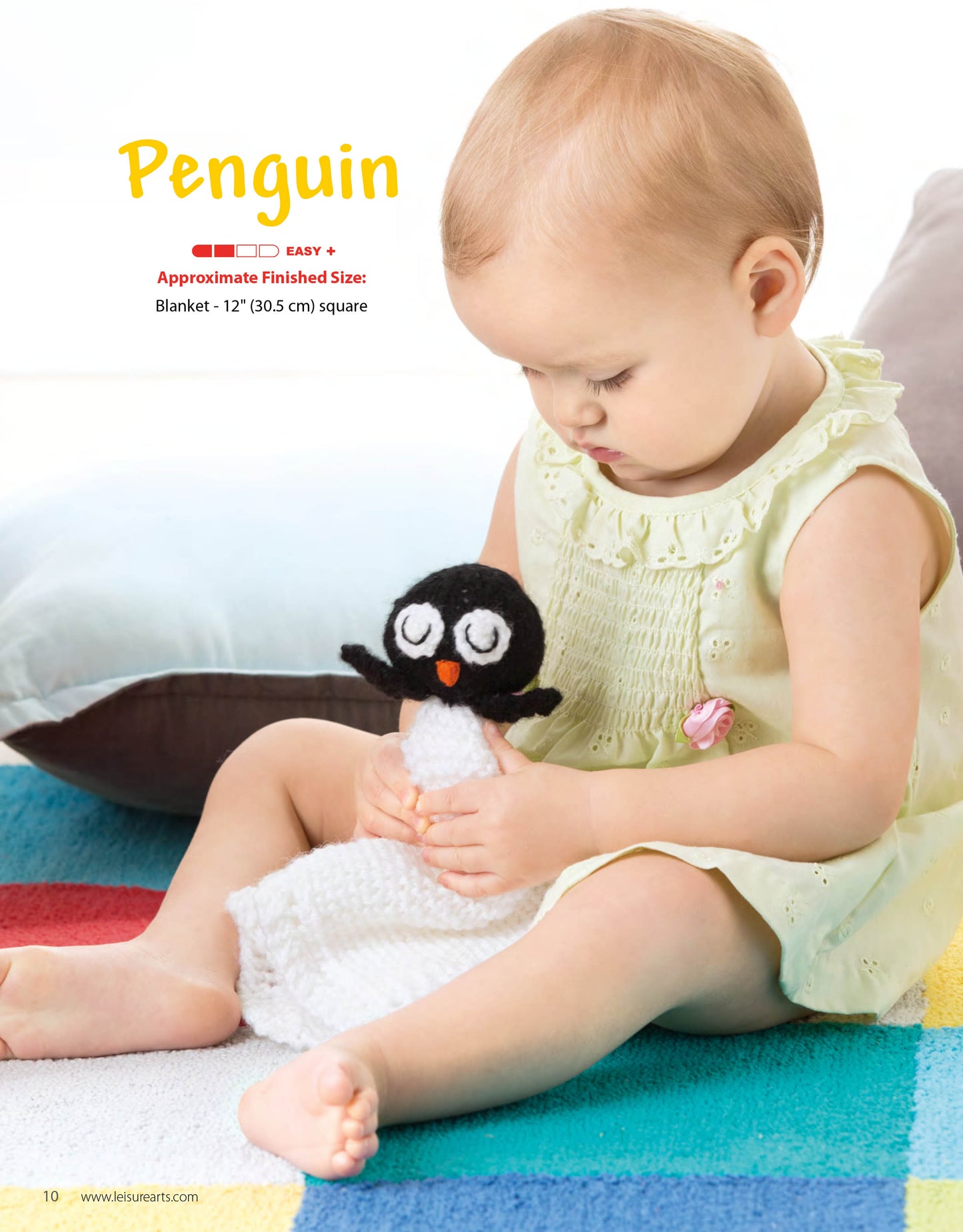 A young child in a pale yellow dress sits on a colorful striped rug, holding an Animal Lovies—Huggable Blanket Buddies toy by Leisure Arts. Bonus! Online tutorials and beginner knitting pattern info for this adorable gift are included above.