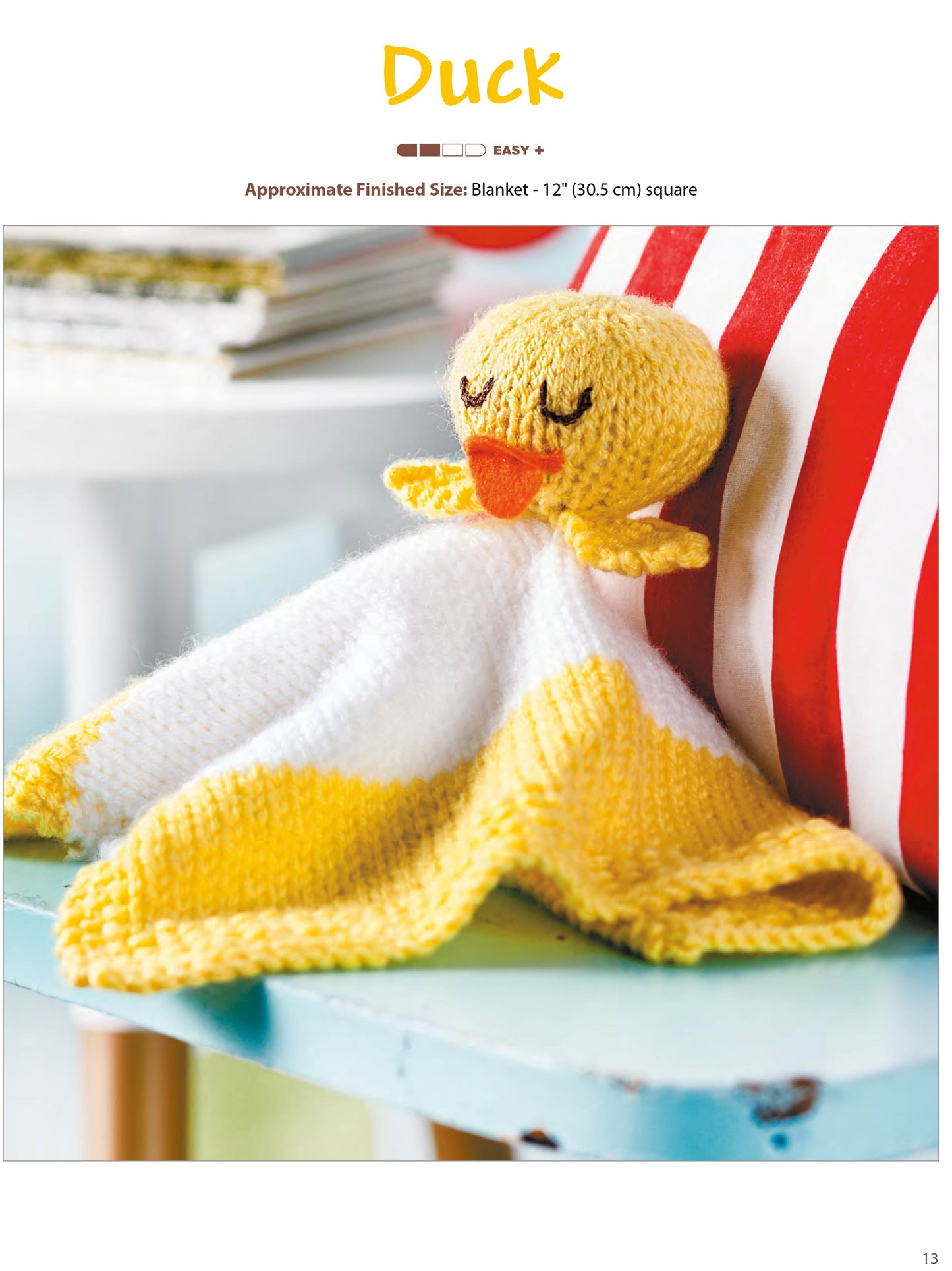 The Leisure Arts Animal Lovies—huggable blanket buddies—make adorable gifts! A yellow duck lovey sits on a light blue chair by a striped cushion, with books blurred in the background. Bonus: includes online tutorials!.