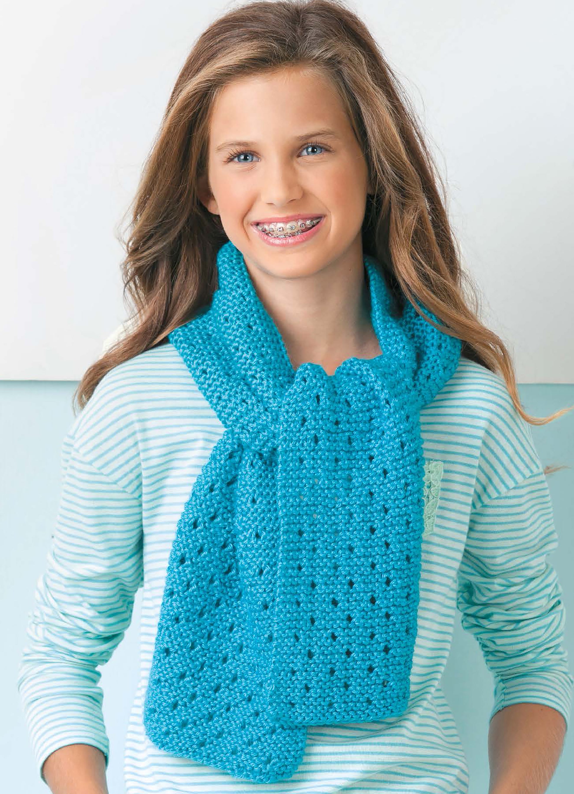 Smiling young person with braces wears a striped shirt and bright blue scarf—great for beginner knitting, as shown in Leisure Arts’ "Cool Stuff Teach Me to Knit—13 Projects for Kids 9-14.
