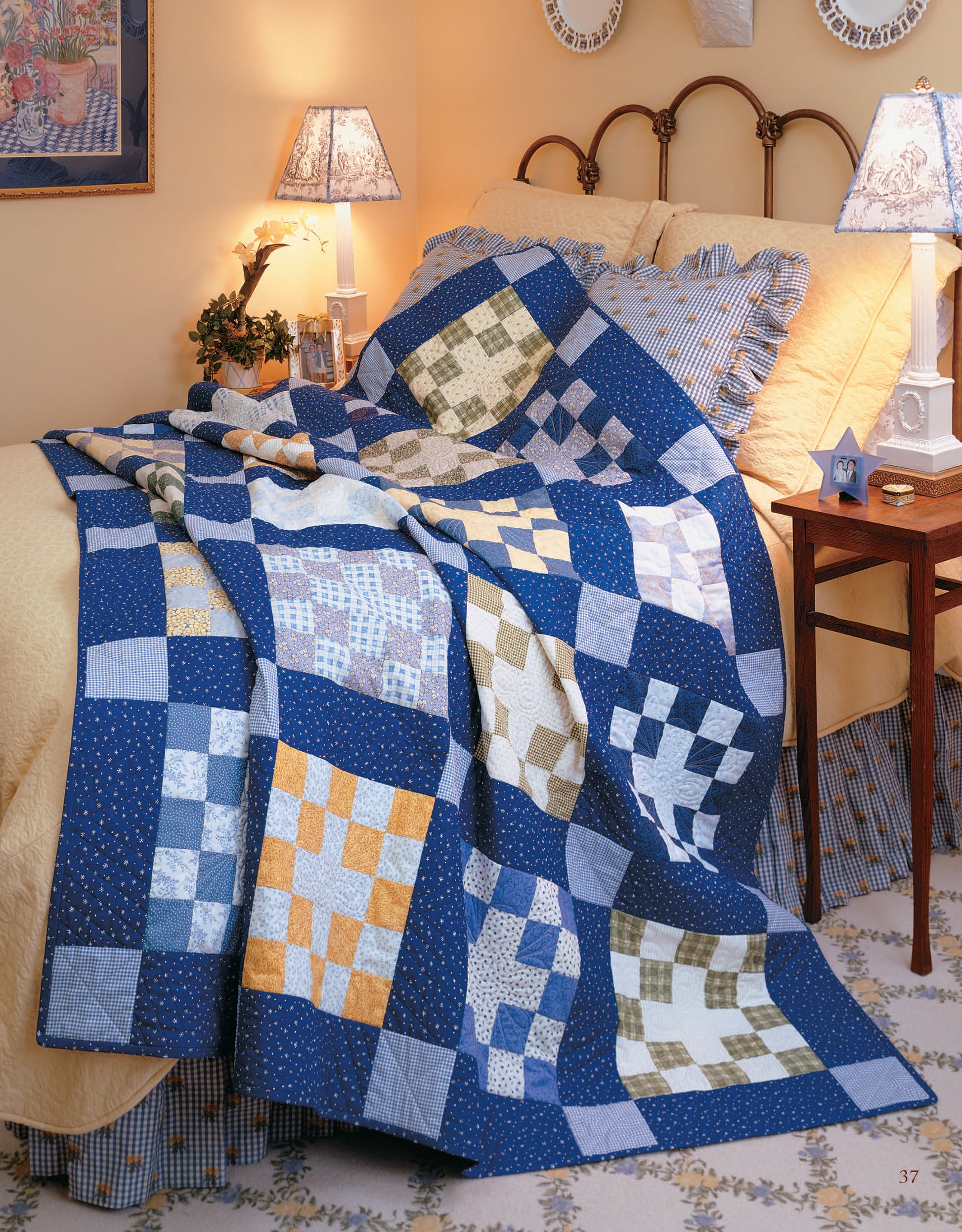 A cozy bedroom features Leisure Arts' Easy Timeless Quilts Digital Download, draped in a colorful blue, white, yellow, and green patchwork beginner quilt over a yellow coverlet with bedside tables and lamps.
