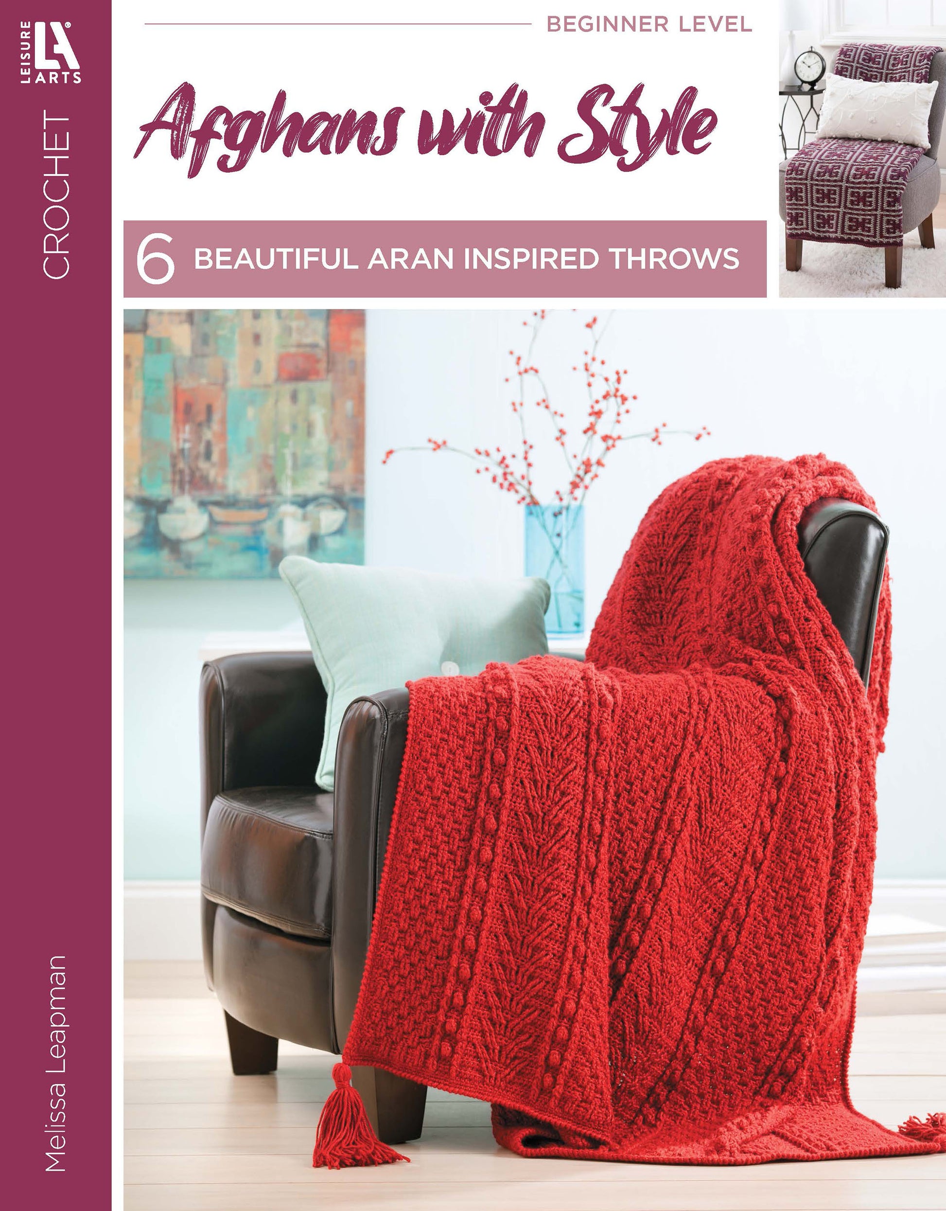 Cover of the Afghans with Style Digital Download by Leisure Arts. A red Aran-inspired crochet throw is draped over a dark armchair beside a light blue pillow and a vase with decorative branches.