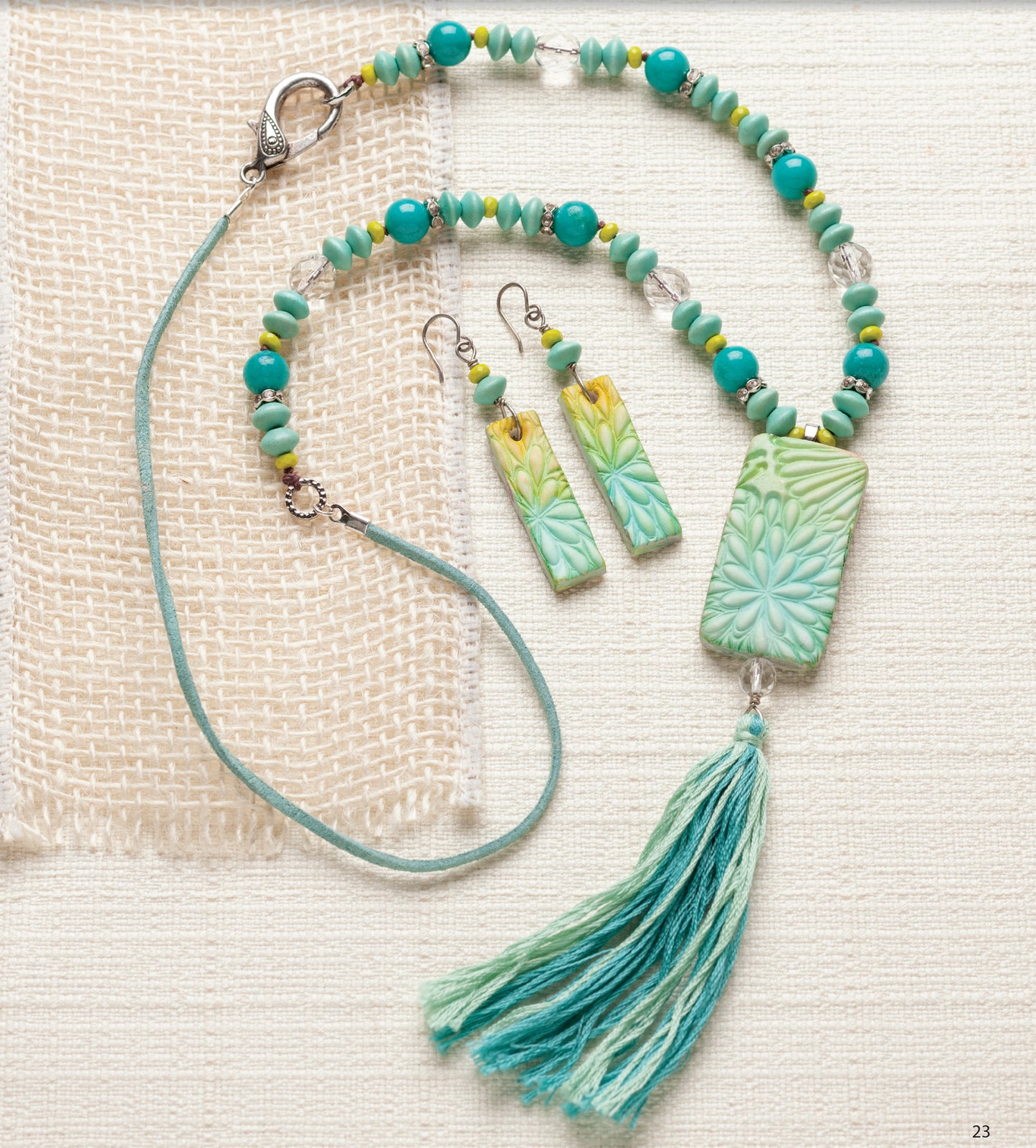 Bold Unique Jewelry by Leisure Arts features a turquoise and green beaded necklace with a floral pendant, matching tassel, and rectangular floral earrings—striking accessories displayed on textured cream fabric.