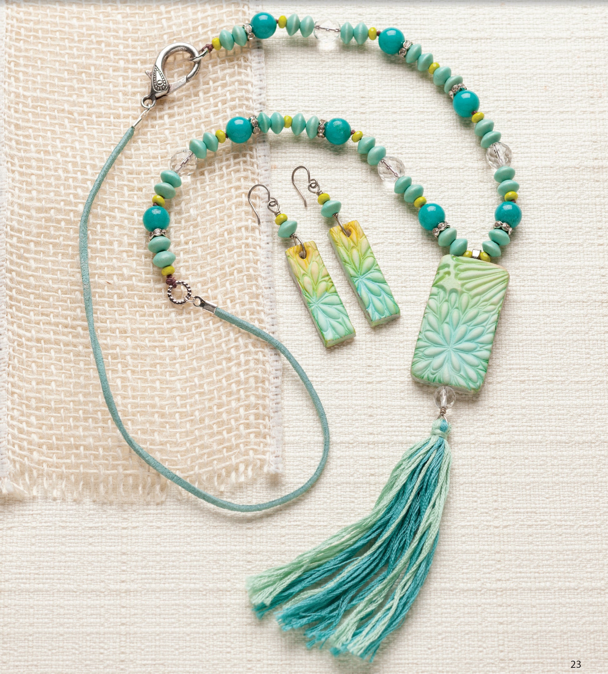 Bold Unique Jewelry by Leisure Arts features a turquoise and green beaded necklace with a floral pendant, matching tassel, and rectangular floral earrings—striking accessories displayed on textured cream fabric.
