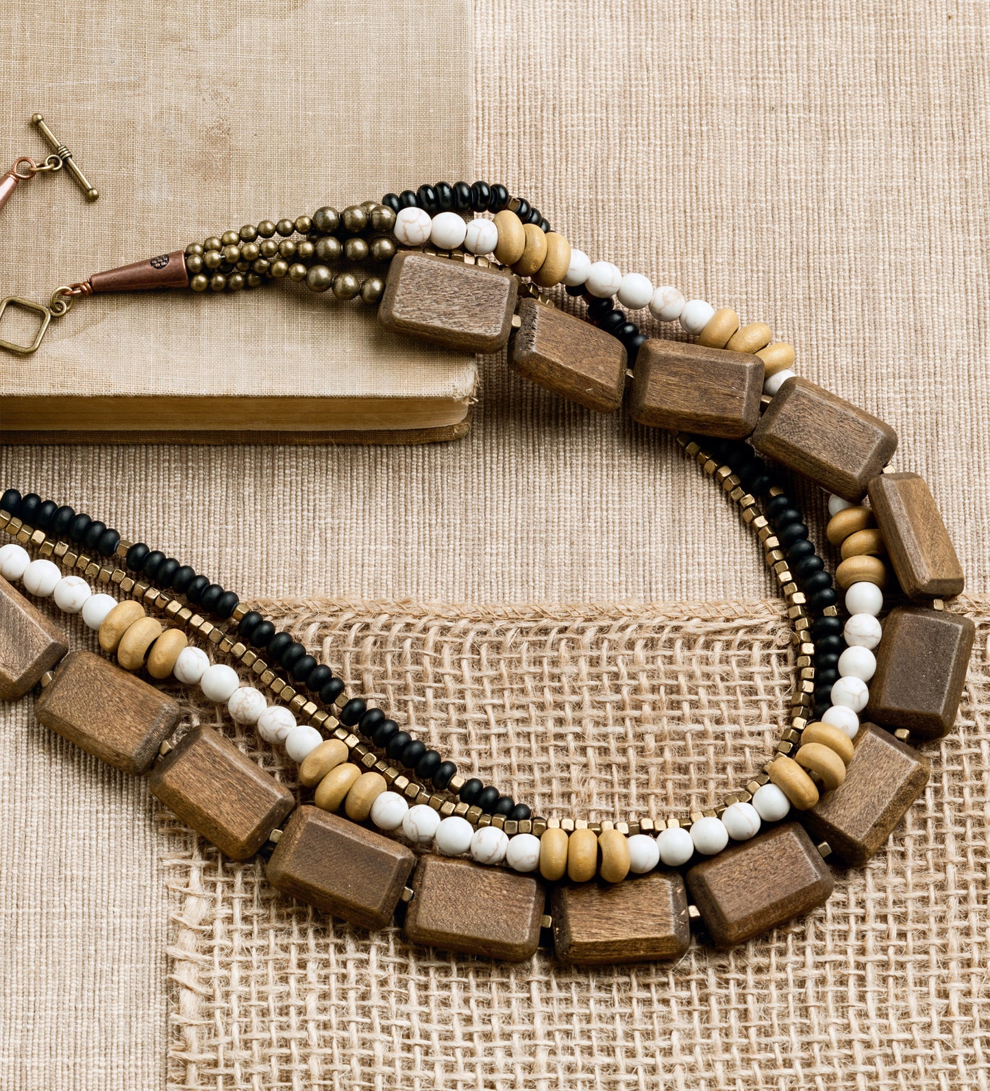 Leisure Arts' Bold Unique Jewelry features a multi-strand necklace with large rectangular wooden beads and small round black, white, gold, and tan beads—an eye-catching fashion statement.