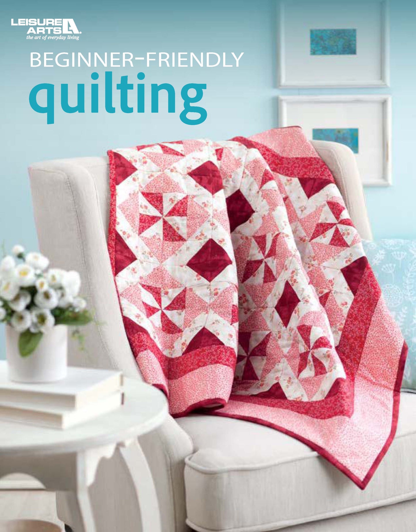 A vibrant pink and white patchwork quilt decorates a beige armchair beside a vase of flowers, set against a blue wall. Text: Leisure Arts Beginner-Friendly Quilting Digital Download.