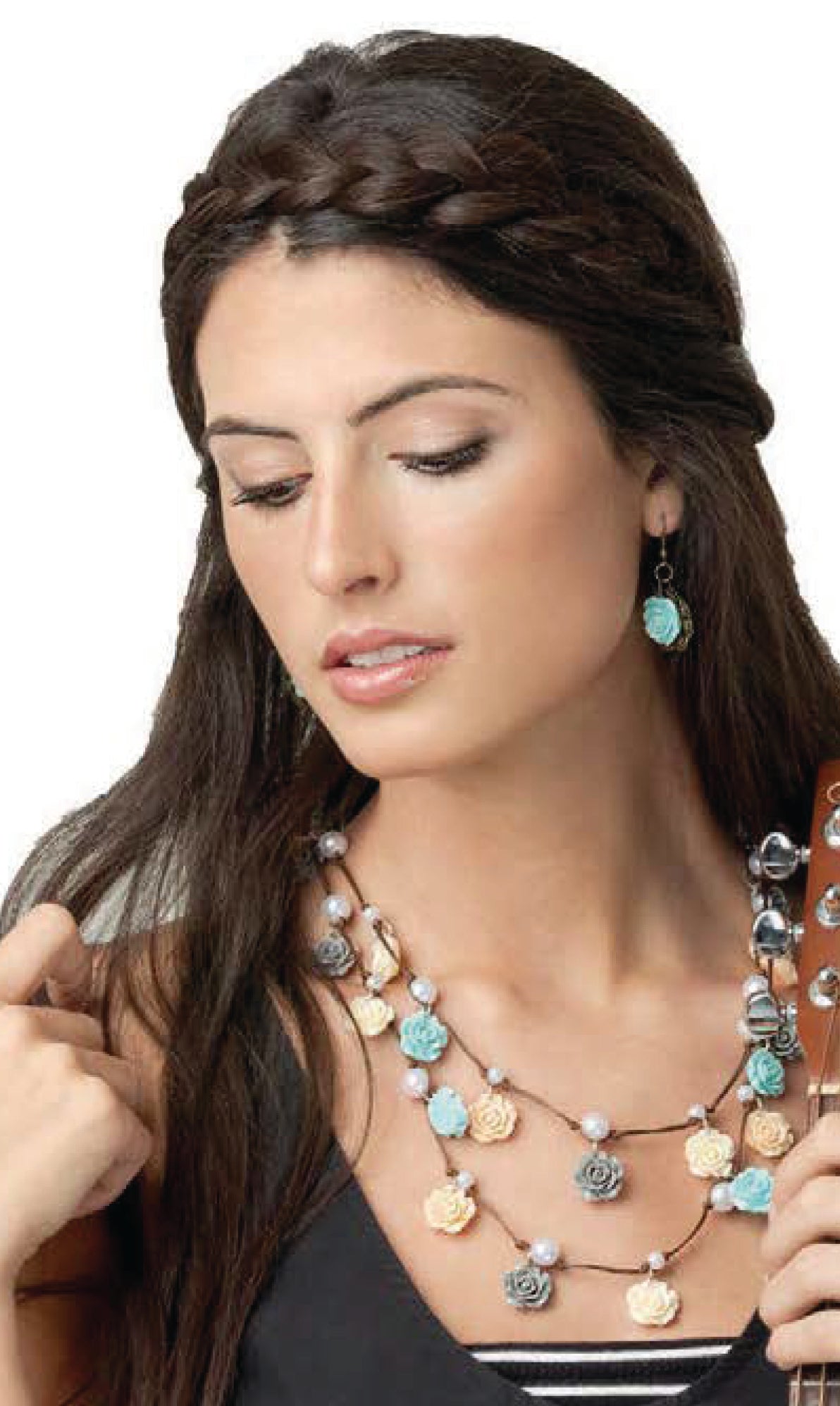 A woman with long brown hair styled in braids wears floral earrings and a pastel-hued layered necklace from the Wanderlust—Travel-Inspired Jewelry collection by Leisure Arts, perfect for mixing and matching, as she looks downward while holding a guitar.