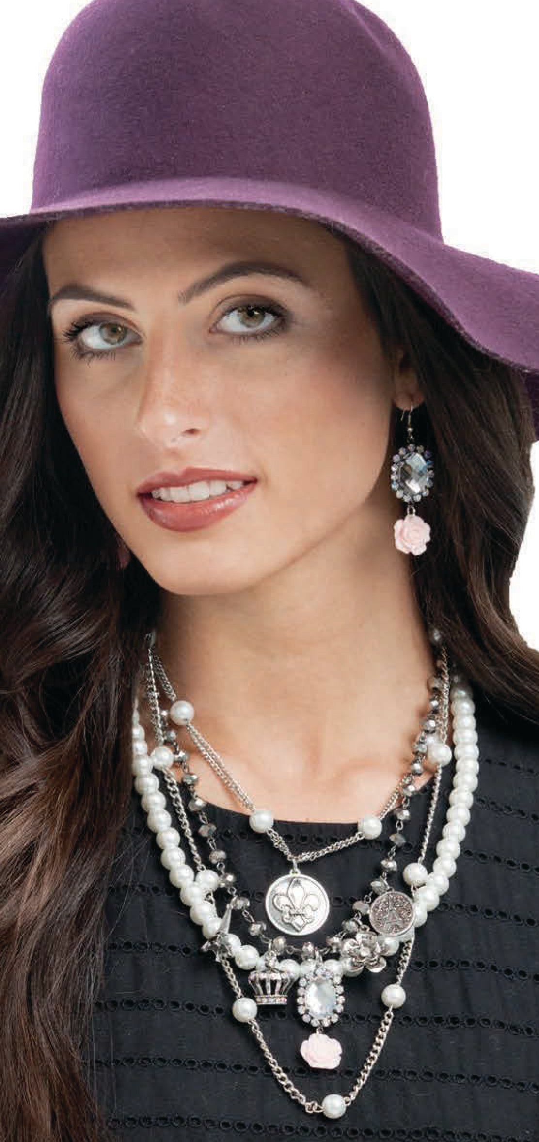 A woman in a purple wide-brimmed hat and bold jewelry—layered pearl and charm necklaces from Leisure Arts' Wanderlust Travel-Inspired Jewelry—gazes sideways, her long dark hair framing a black textured top.