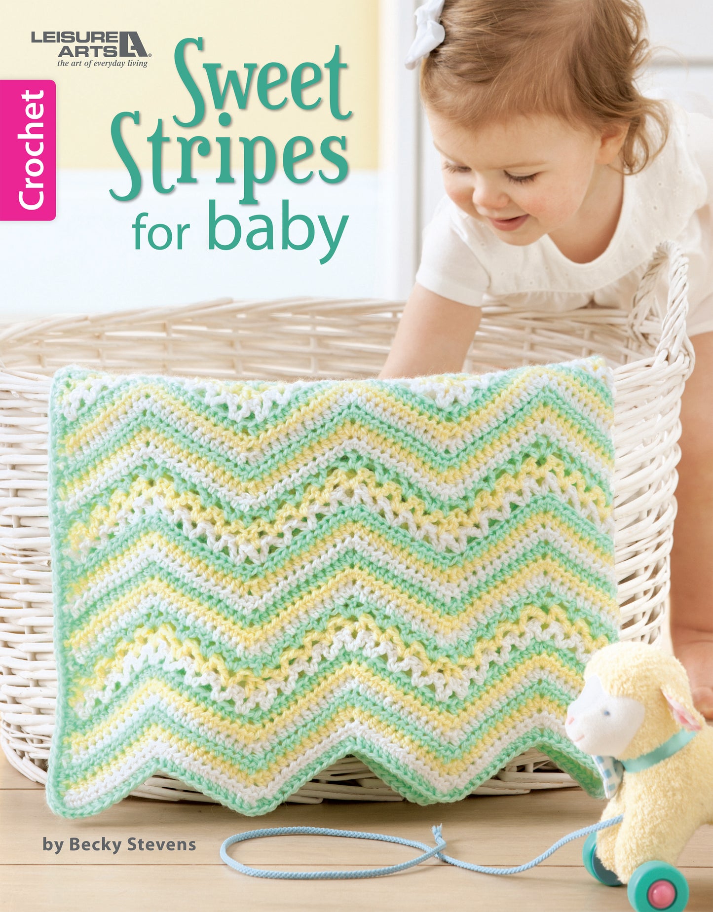 A smiling baby leans over a white basket, admiring the pastel-striped afghan from Leisure Arts' "Sweet Stripes for Baby—Make 3 Color Afghans." A yellow plush lamb with a blue leash sits nearby. Text reads: Sweet Stripes for Baby.