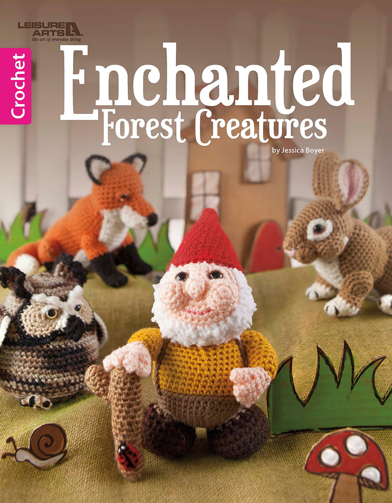 The Enchanted Forest Creatures to Crochet Digital Download from Leisure Arts features woodland animals—gnome, rabbit, raccoon, and fox—among mushrooms and trees, with step-by-step crochet patterns and instructions for each charming figure.