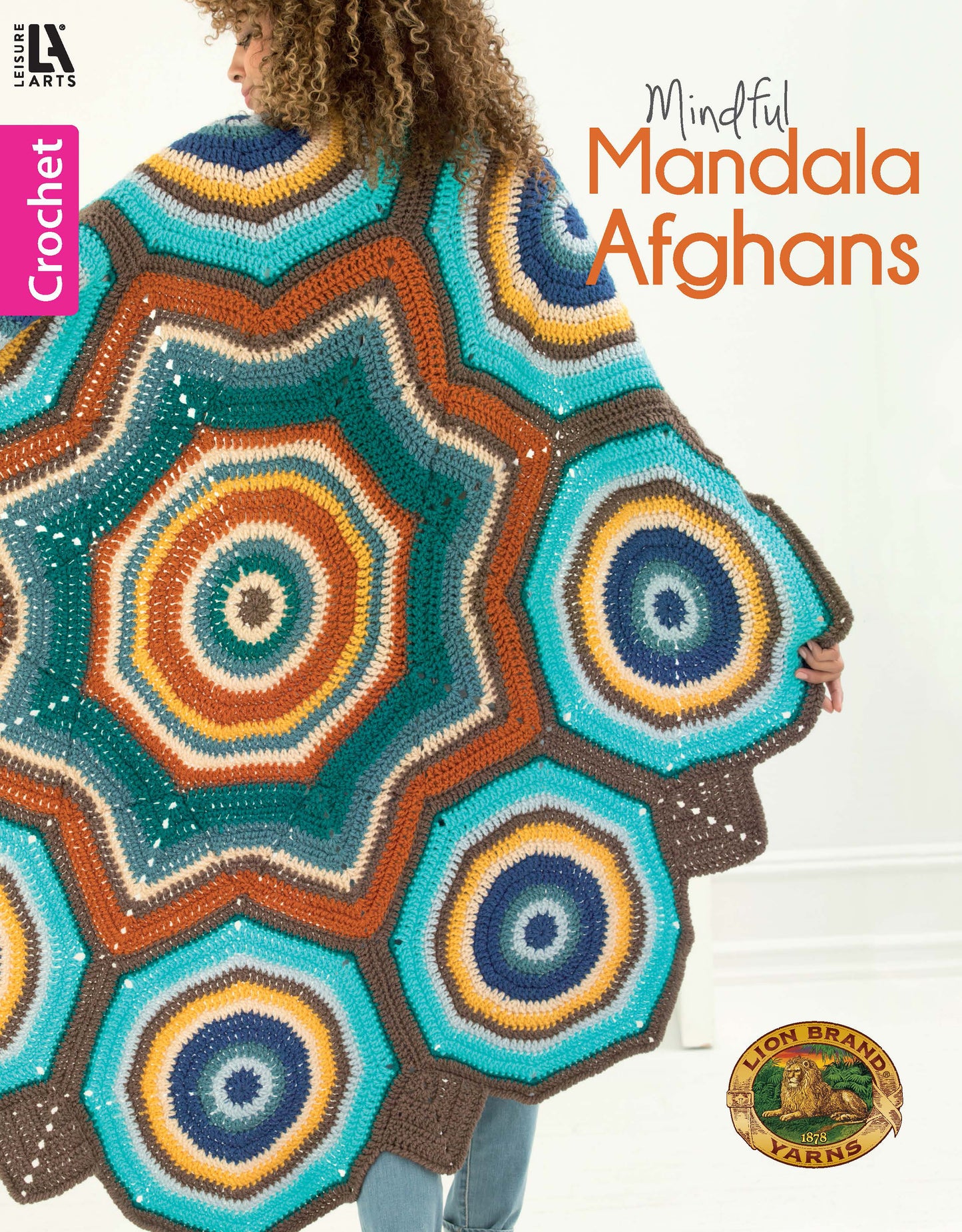 A person wears a vibrant, hexagonal-patterned mandala afghan in teal, orange, brown, and cream. Cover text: Mindful Mandala Afghans by Leisure Arts—featuring inspiring crochet patterns for all skill levels.