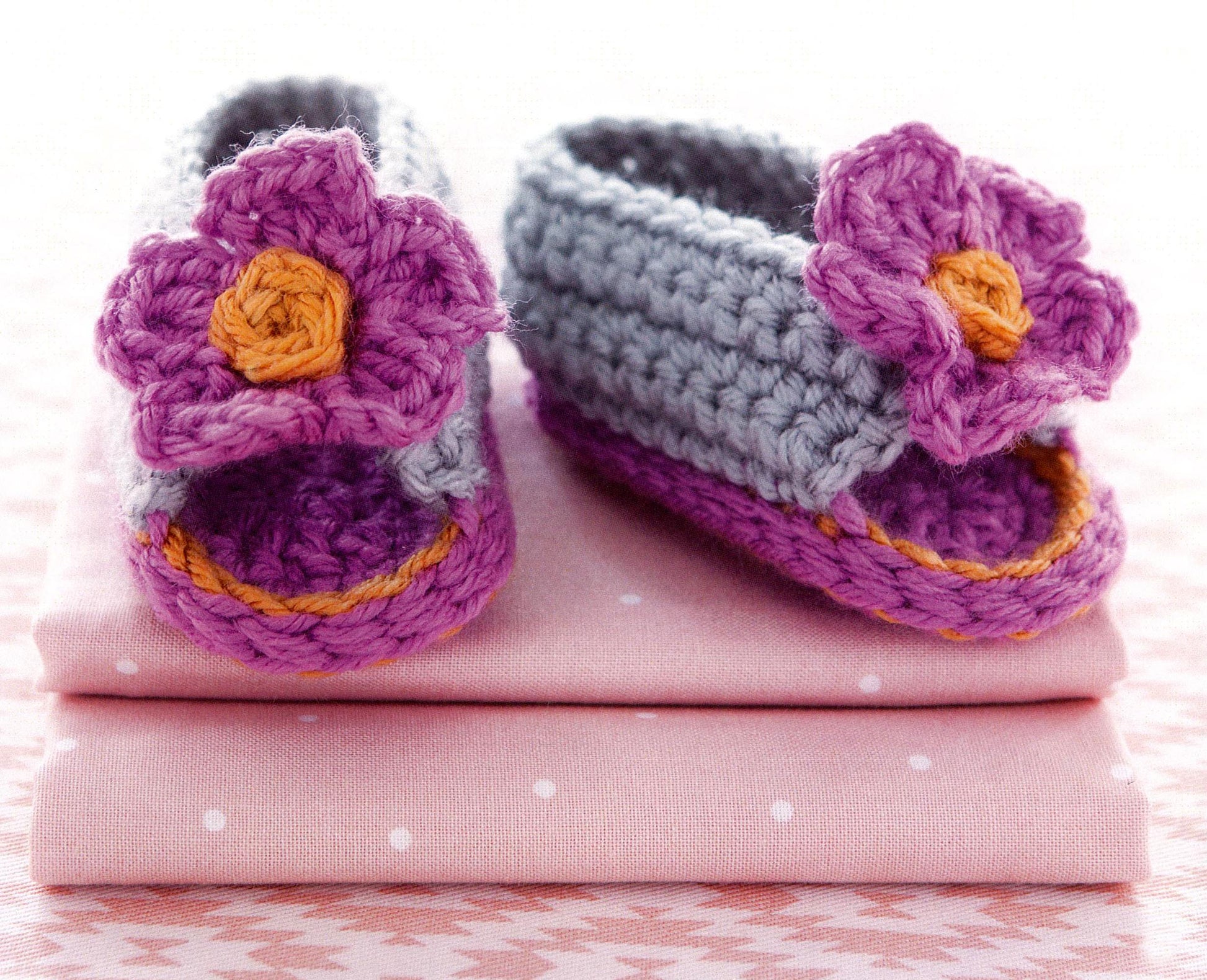 The Modern Baby Booties Digital Download by Leisure Arts features beginner crochet patterns for adorable purple and gray booties with orange flower details, perfect for creating charming handmade baby shoes.