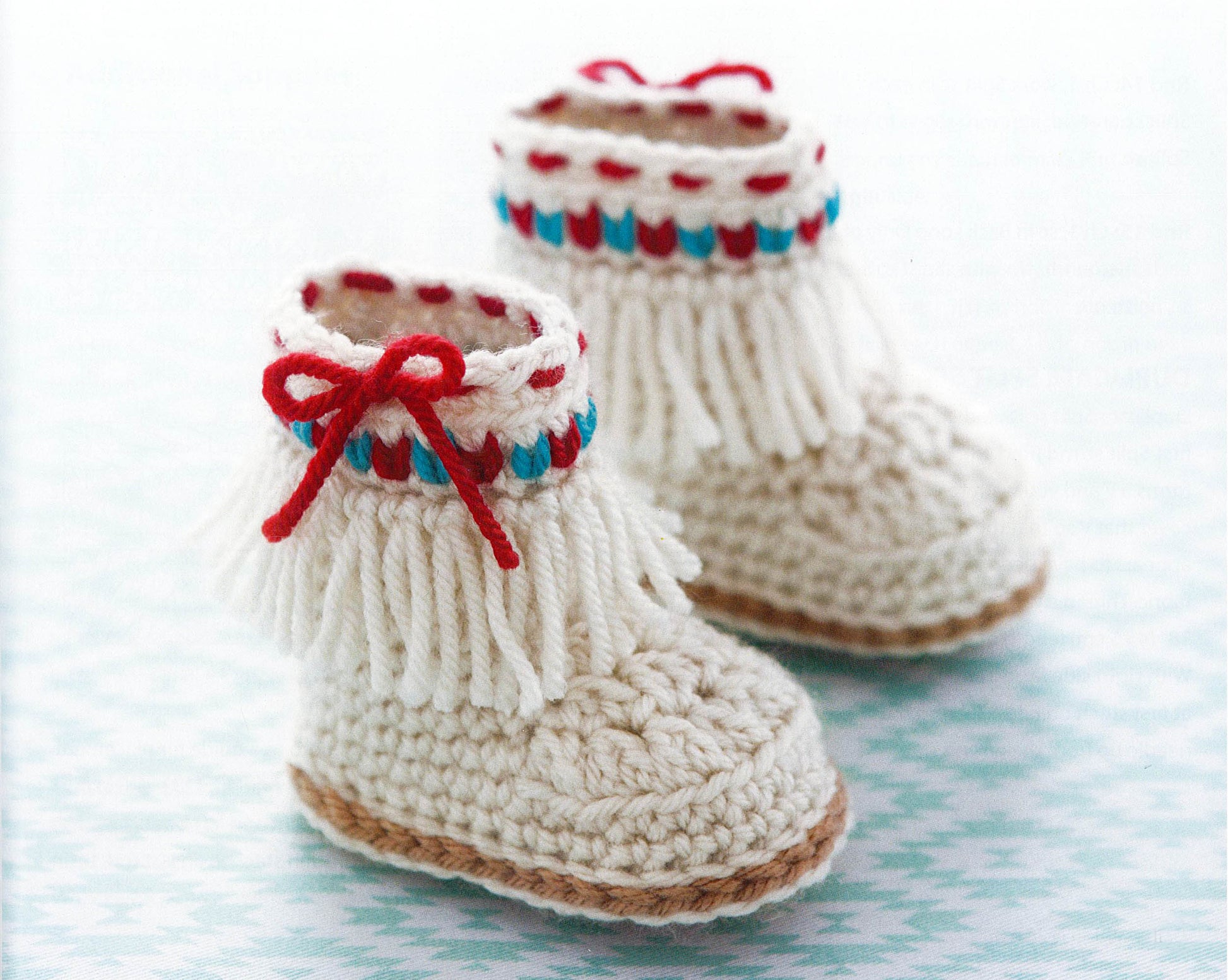 Modern Baby Booties Digital Download by Leisure Arts—cream crocheted booties with fringe, red and blue accents, and red yarn bows. Perfect for those seeking easy baby shoe or beginner crochet patterns.