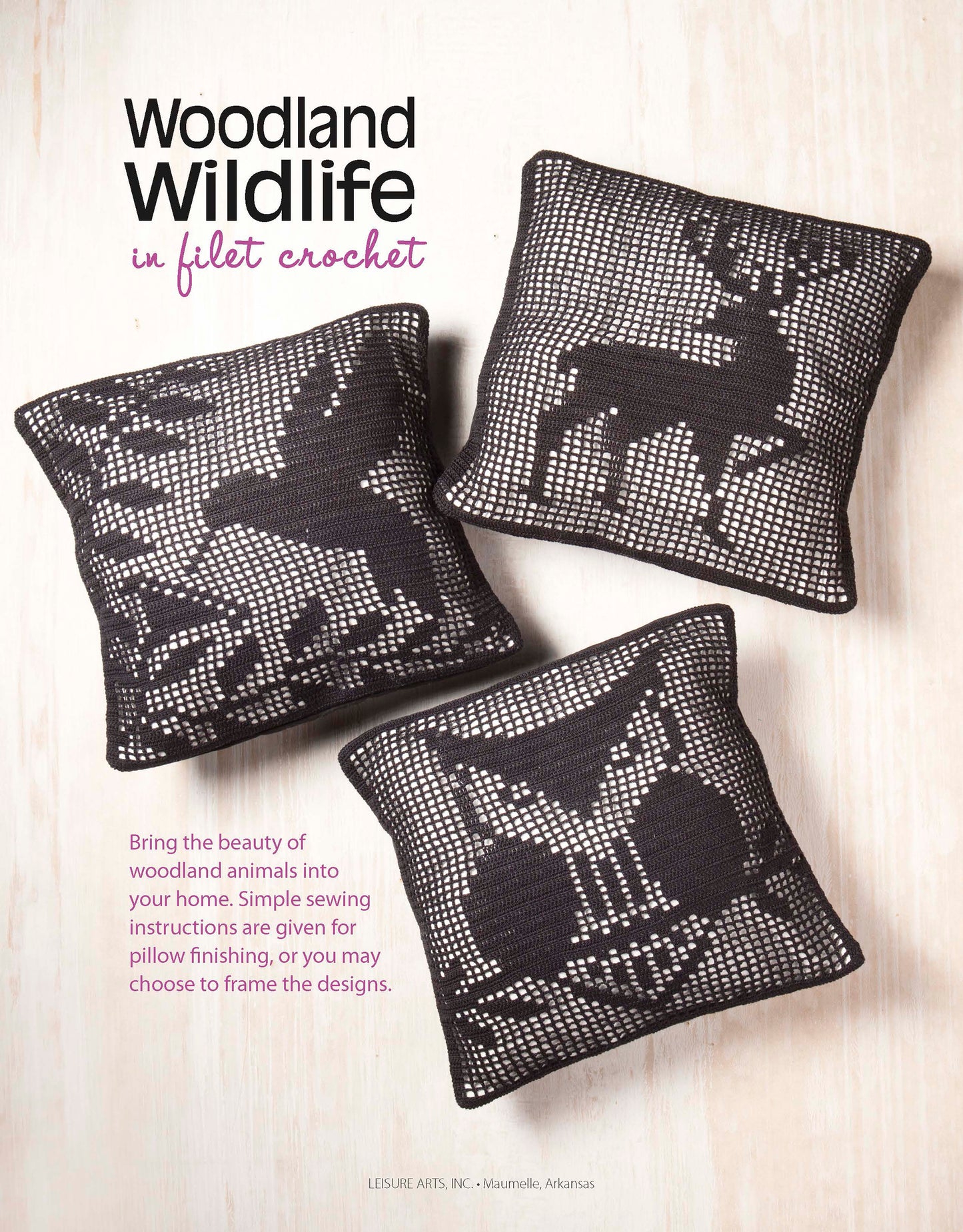 Three square pillows with black and white filet crochet patterns featuring a squirrel, deer, and owl from the Leisure Arts "Woodland Wildlife in Filet Crochet" collection are displayed on a light wooden surface.