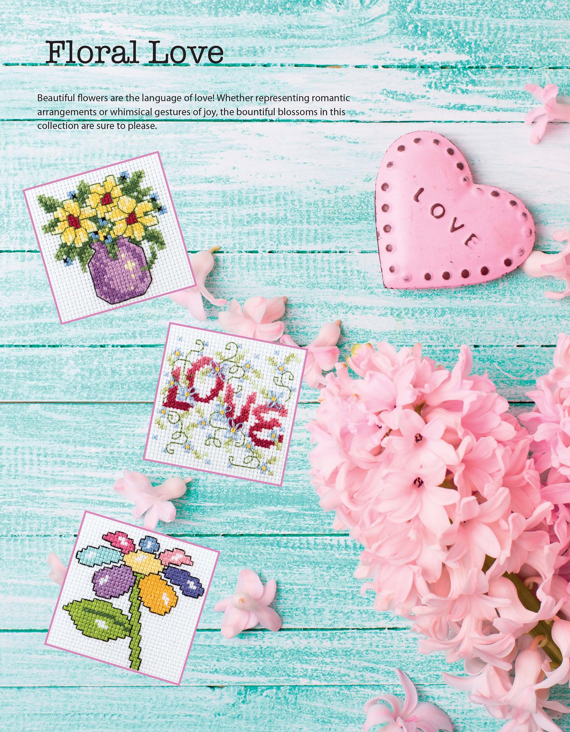 Three small floral cross stitch designs from "50 Cross Stitch Quickies Flowers and Fun" by Leisure Arts, including a pink heart-shaped LOVE macaron, are displayed on turquoise wood with pink flowers—perfect for beginner cross stitchers.