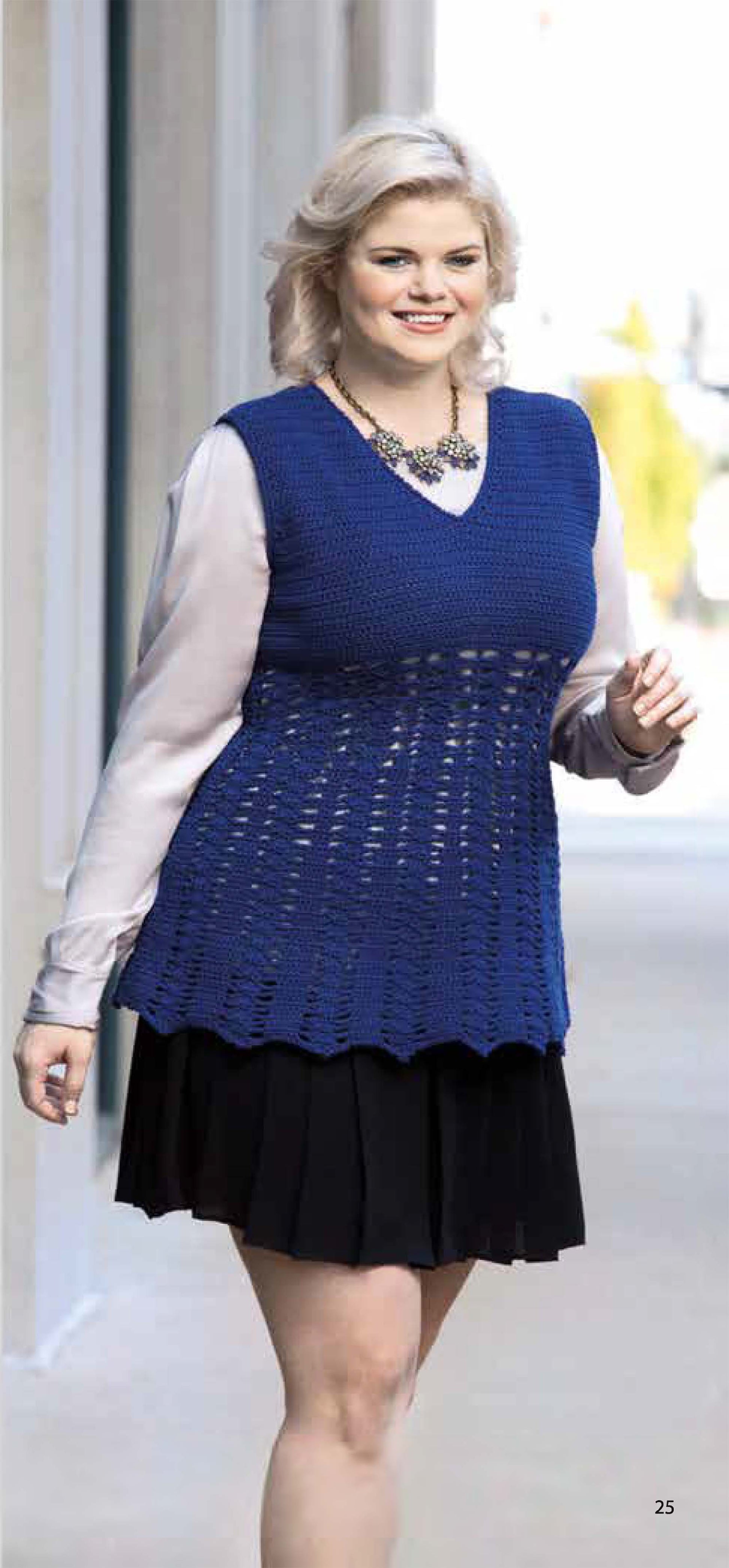 A smiling woman with light blonde hair models a blue vest from "Plus-Size Garments with Style" by Leisure Arts, layered over a light blouse with a black pleated skirt and necklace, walking outdoors near a building.
